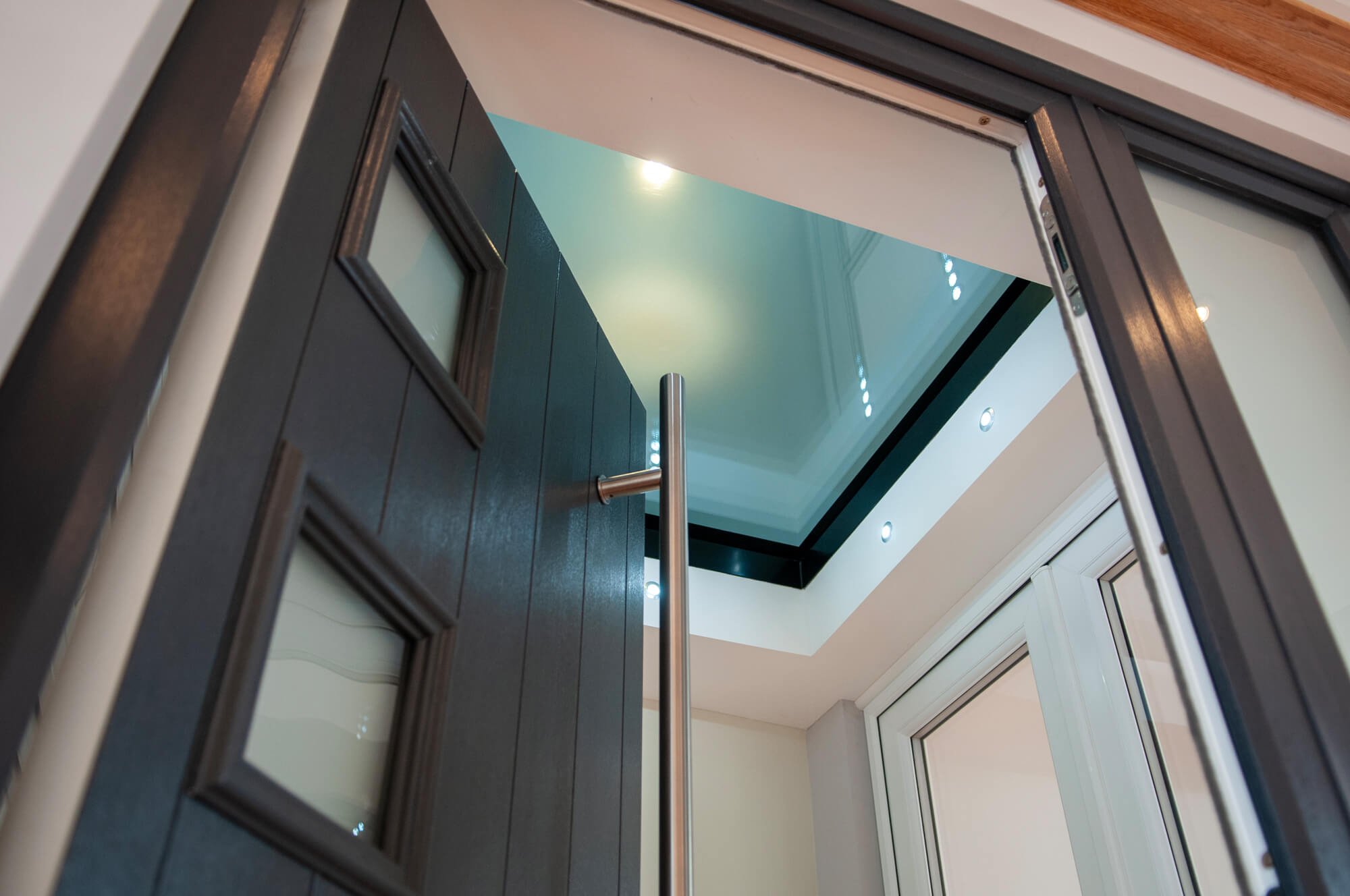 View looking up at a modern interior with a dark door, a small window, a metallic handrail, a skylight or ceiling window, and recessed ceiling lights.