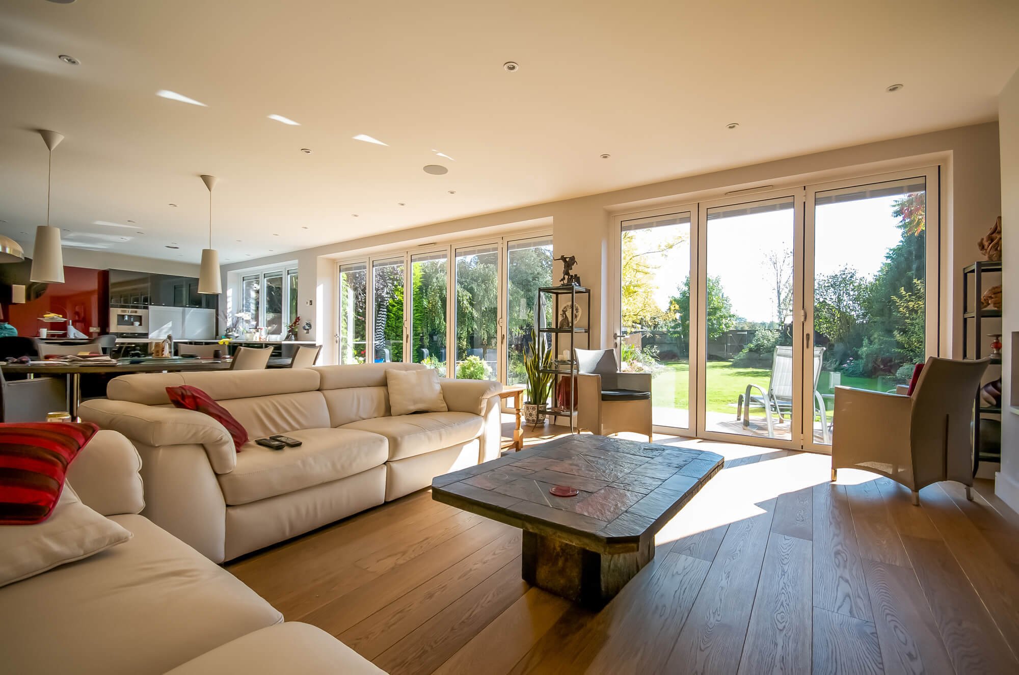 Bright living room with large sliding glass doors opening to a green backyard, beige sofas, and a rustic wooden coffee table.