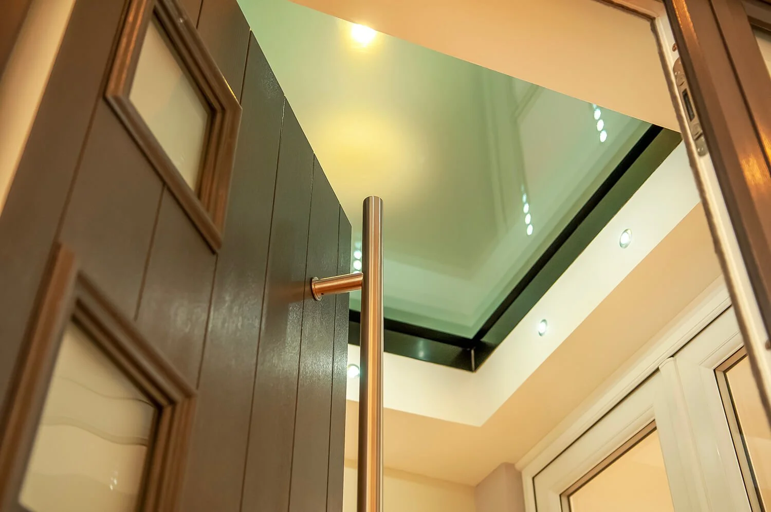 View from the ground looking up at an interior ceiling with recessed lighting, a rectangular glass skylight, and nearby window frames.