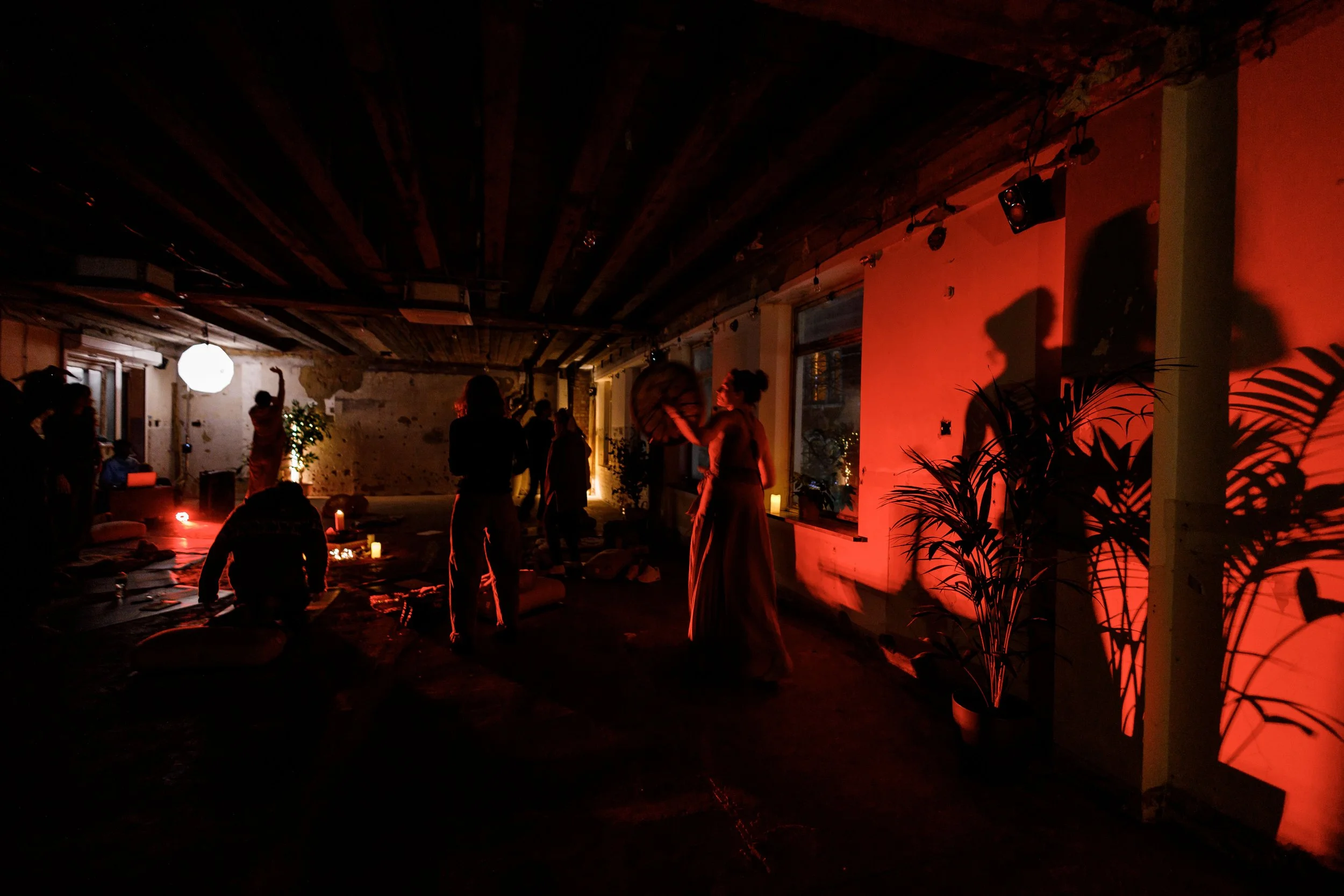 A dimly lit indoor gathering with people dancing and socializing, warm lighting, candles, and plants, creating a cozy atmosphere.