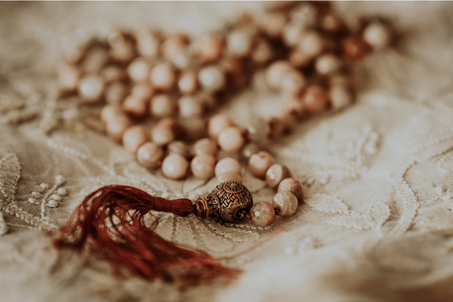 Close-up of a beaded necklace with a decorative metal bead and a red tassel, resting on embroidered fabric.