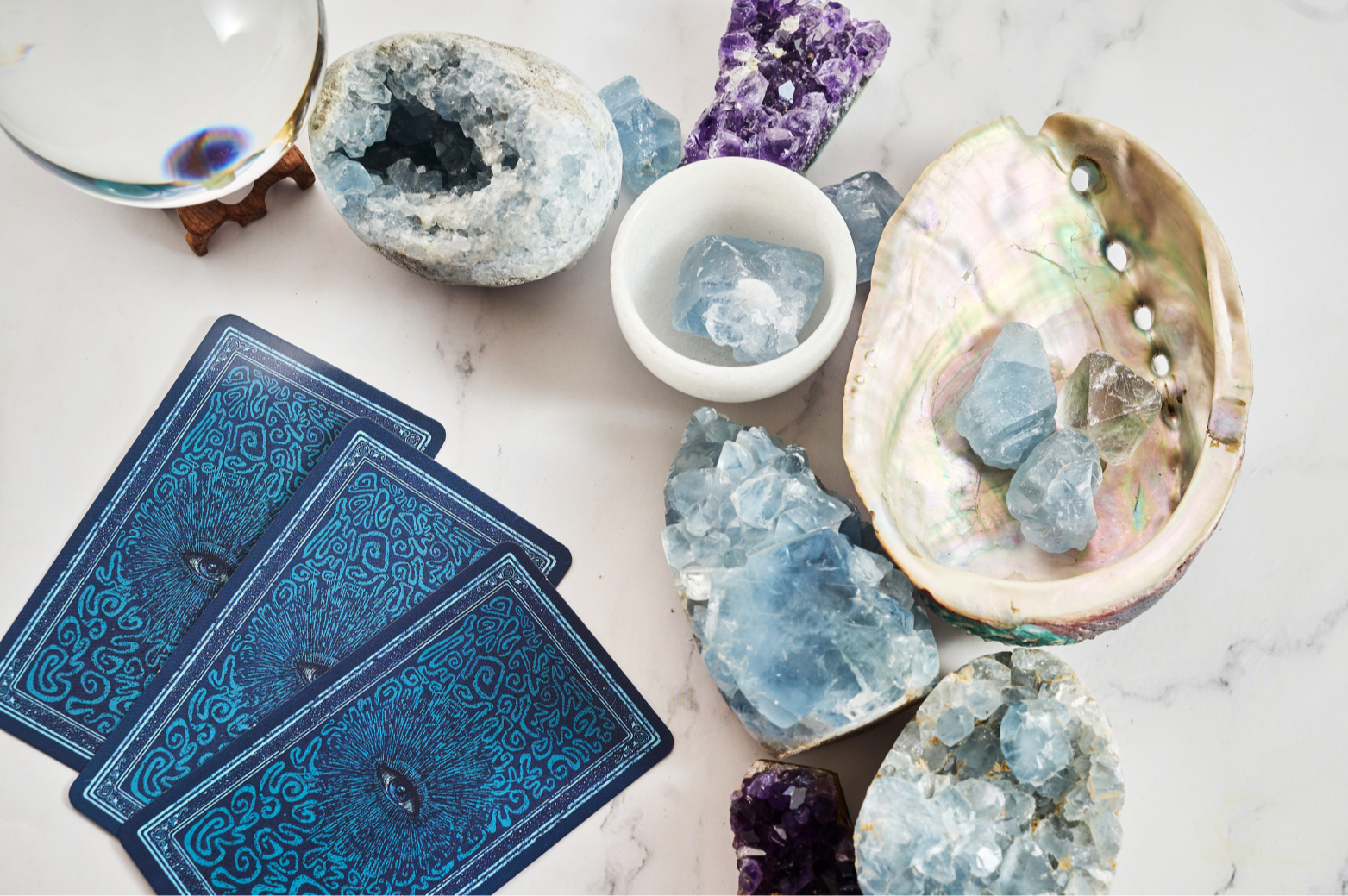 A set of tarot cards, various healing crystals, a shell, and a glass of water on a white surface.