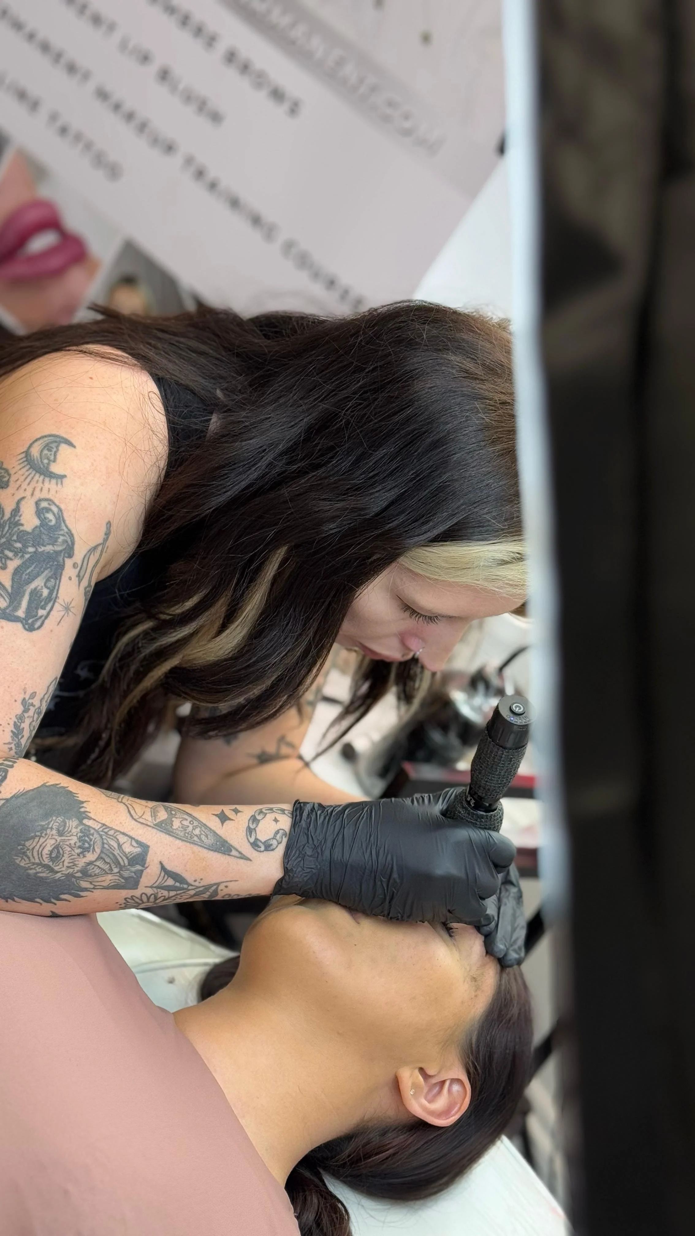 Tattooed artist performing a tattoo on a woman's arm in a tattoo studio, with tattoo supplies on the table. Permanent make up, cosmetic tattooing