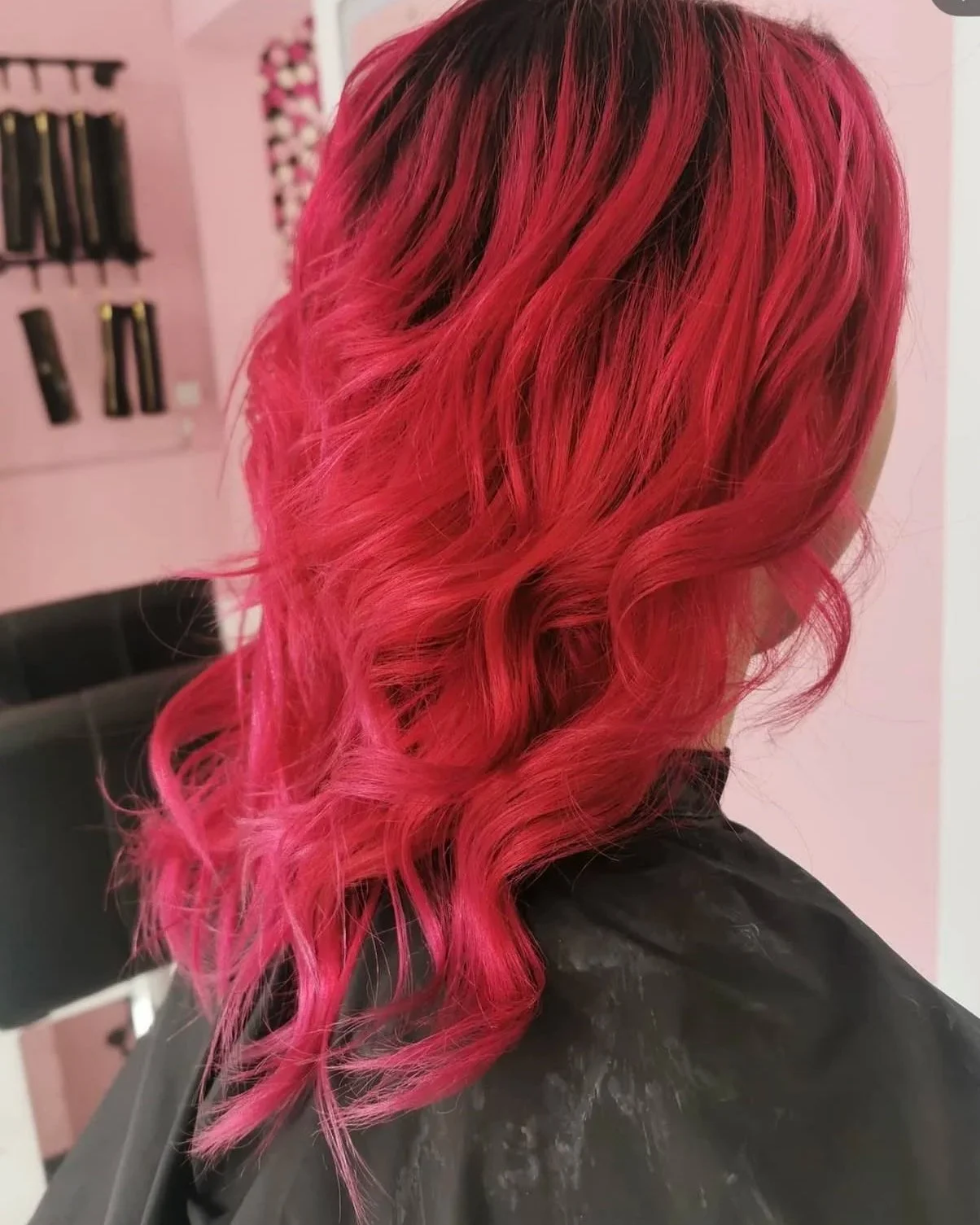 Woman with bright pink, wavy hair sitting in a salon chair.