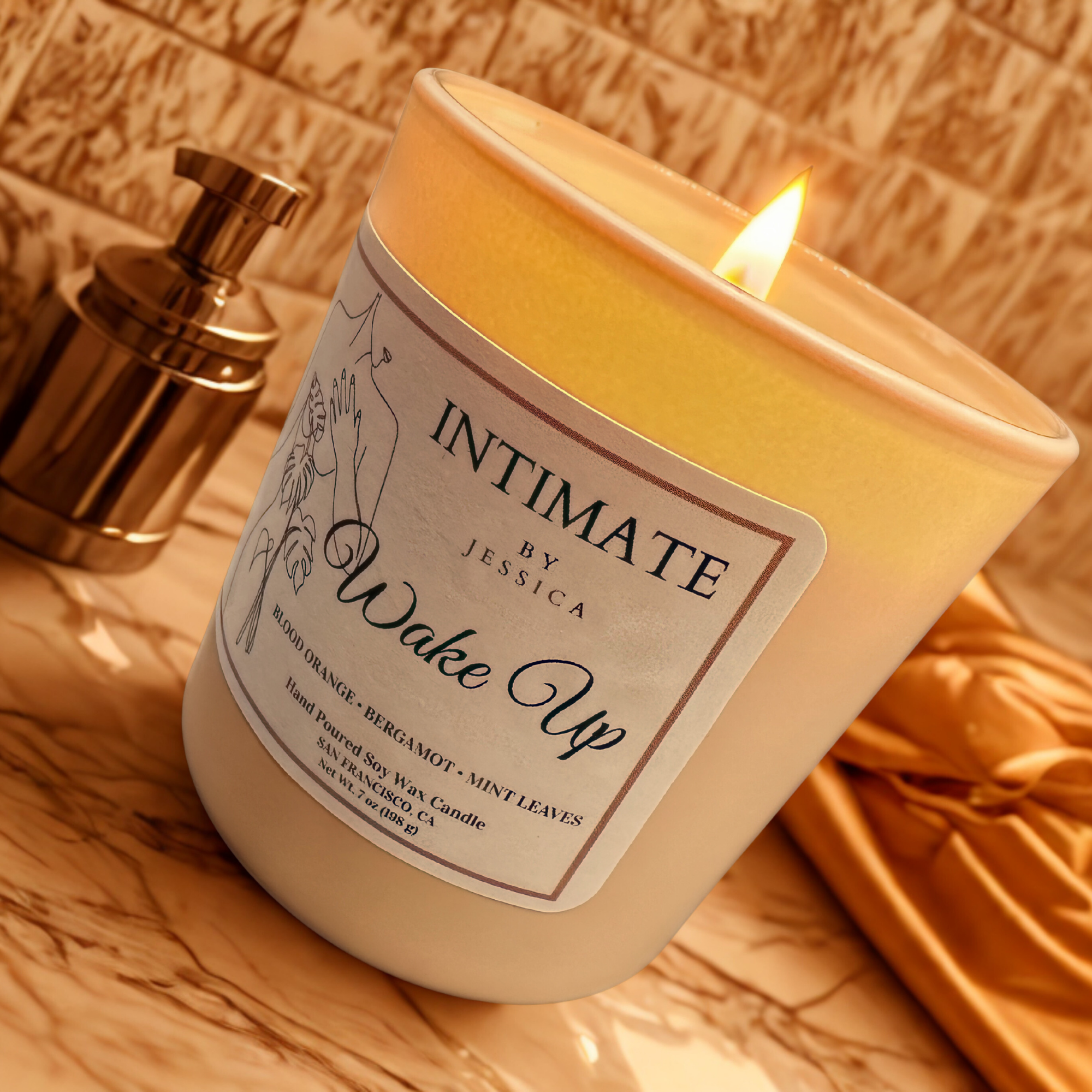A lit orange candle with a floral and botanical label, placed on a wooden surface with a brass lamp in the background.