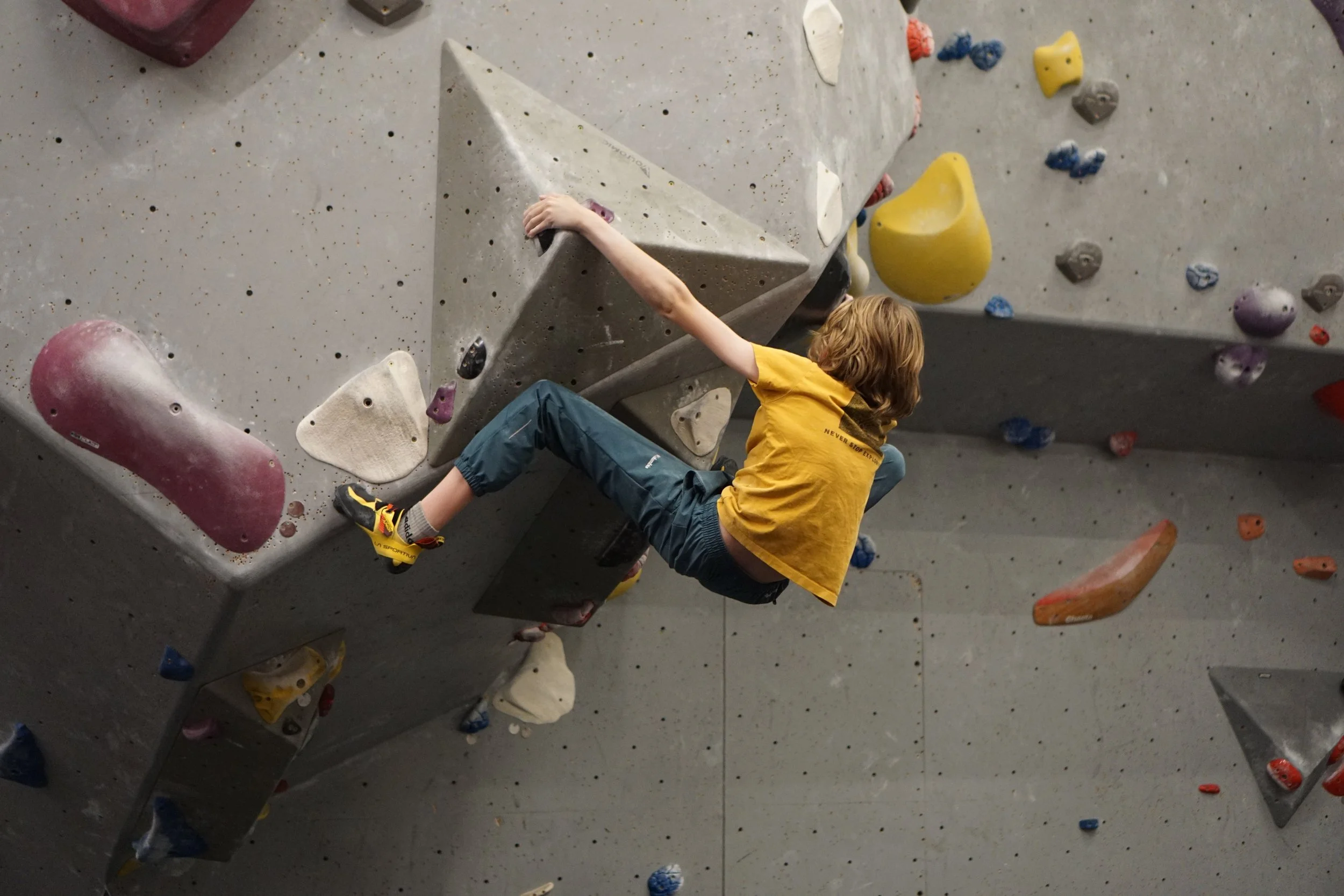 A young boy climbing on an indoor rock climbing wall, gripping holds with his hands and feet.
