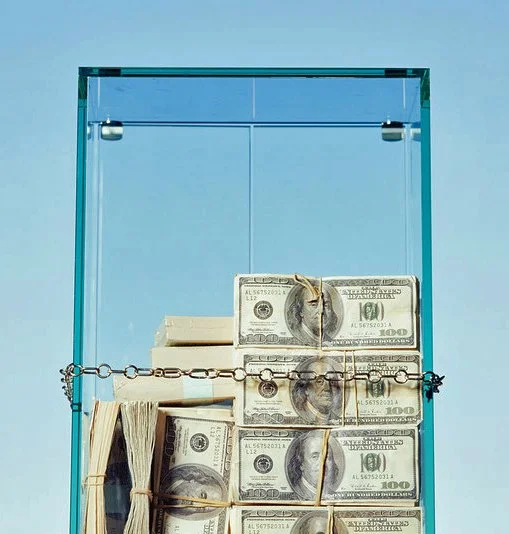 Box filled with stacked hundred-dollar bills secured with small chains, against a light blue background.