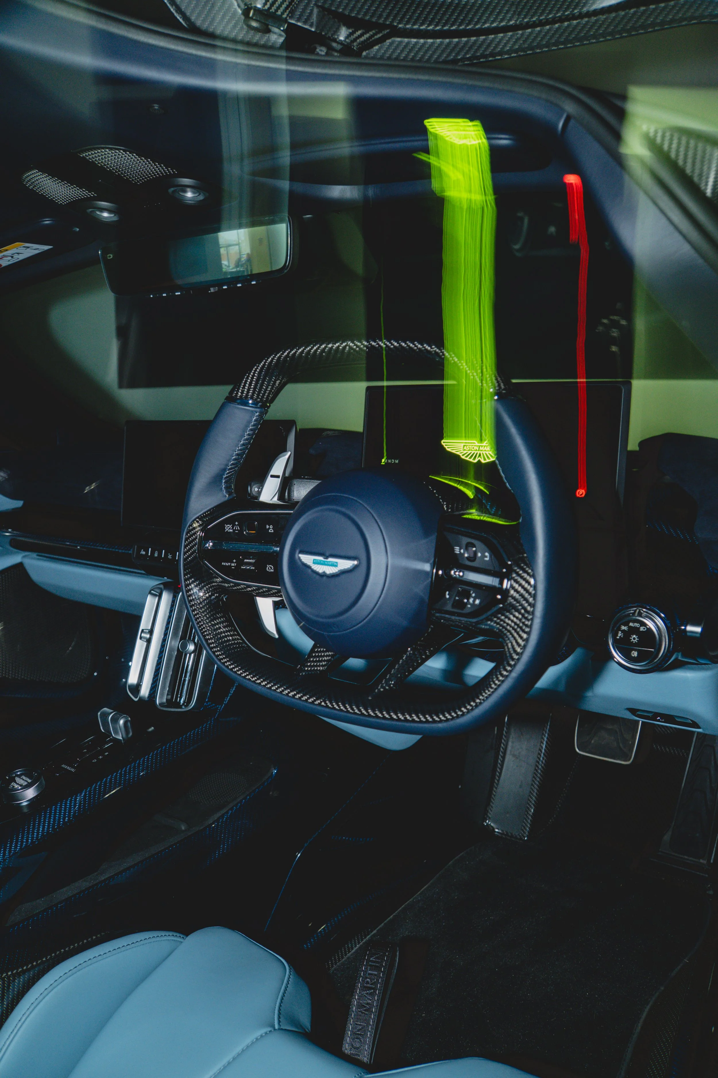 Interior of a luxury car with carbon fiber steering wheel and dashboard, digital display, and black leather seats with light blue cushioning.