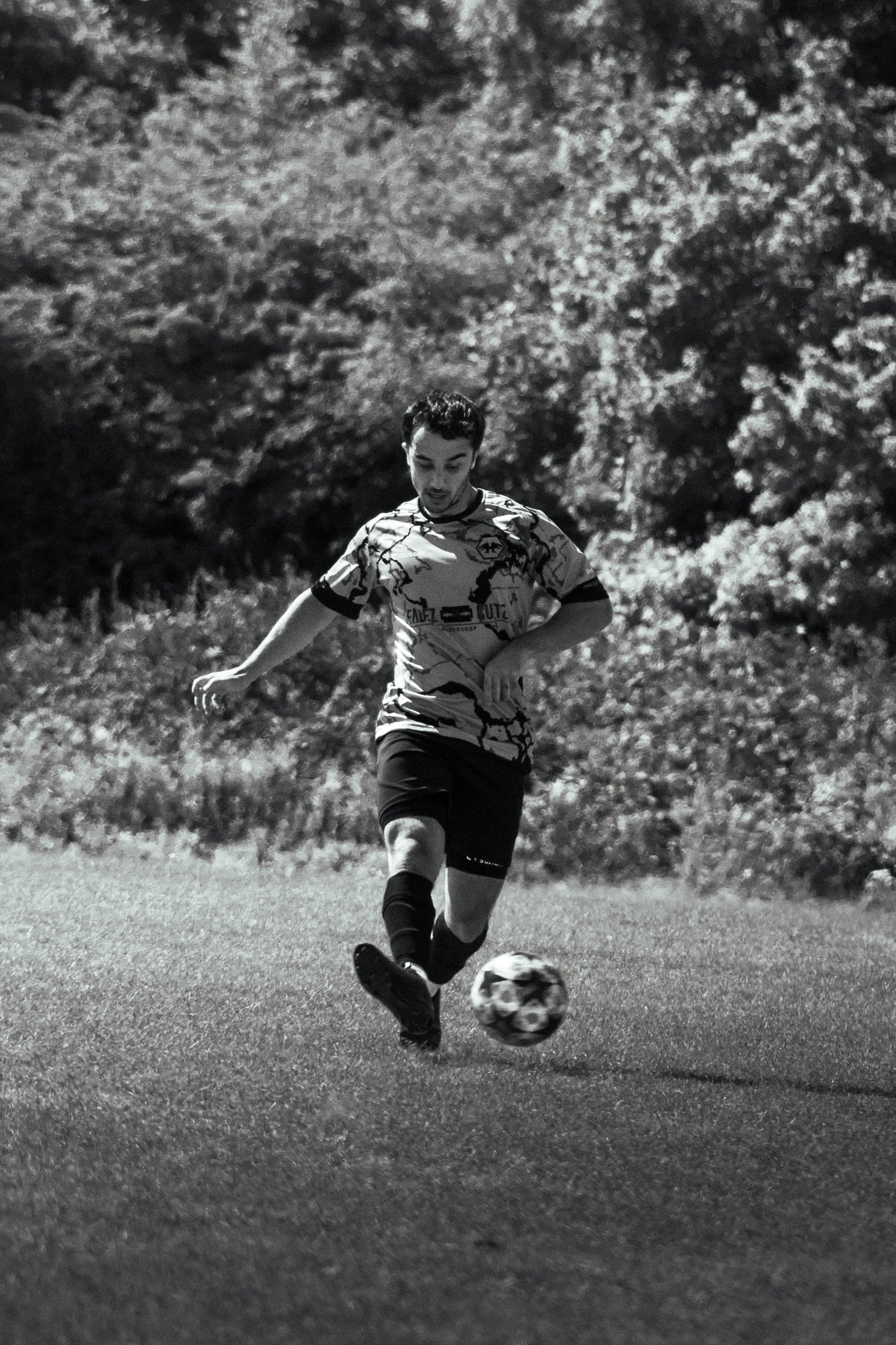 A man playing soccer on a field with trees in the background, black and white photo.