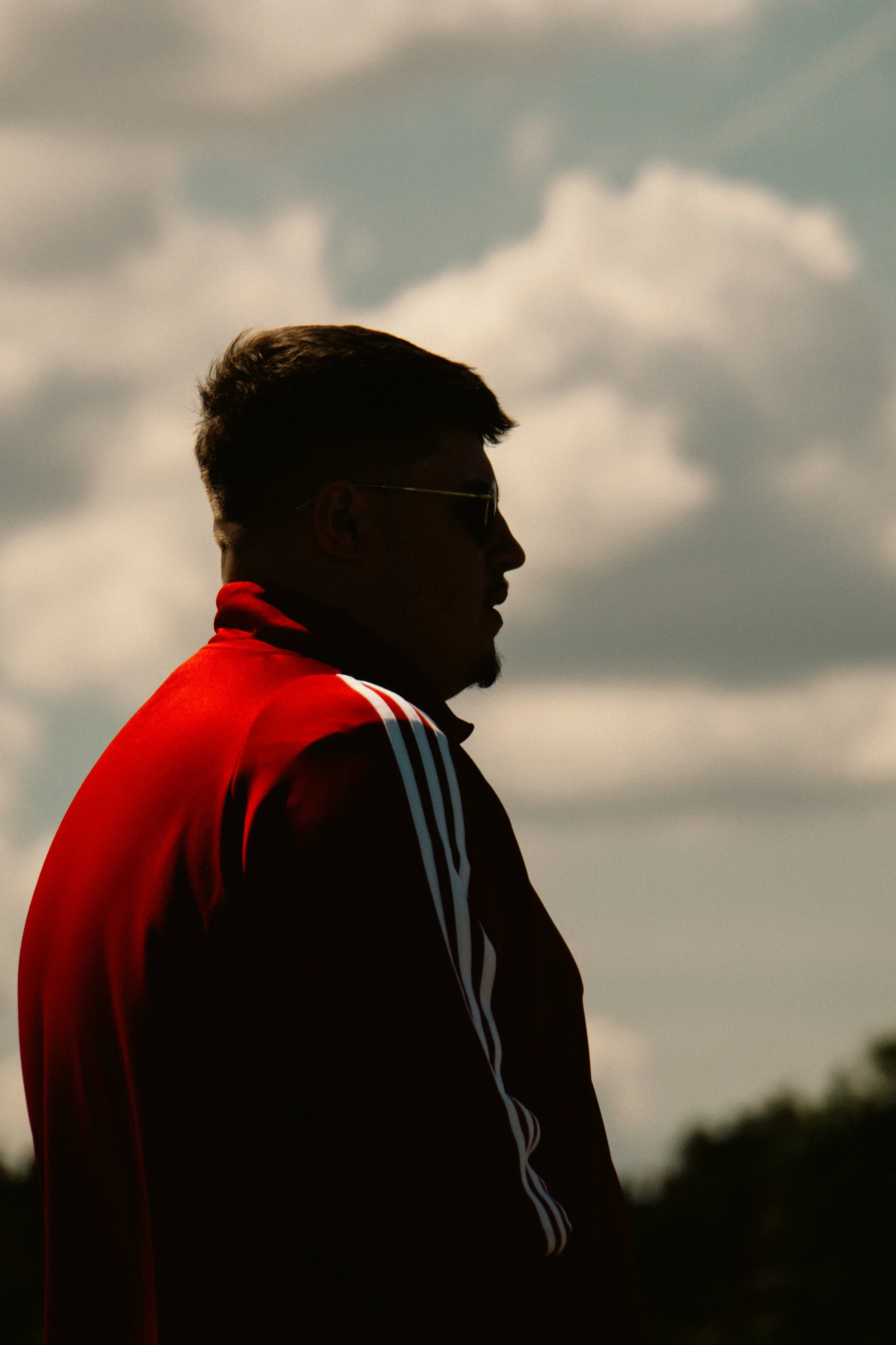 Silhouette of a man with sunglasses and a red jacket against a cloudy sky.