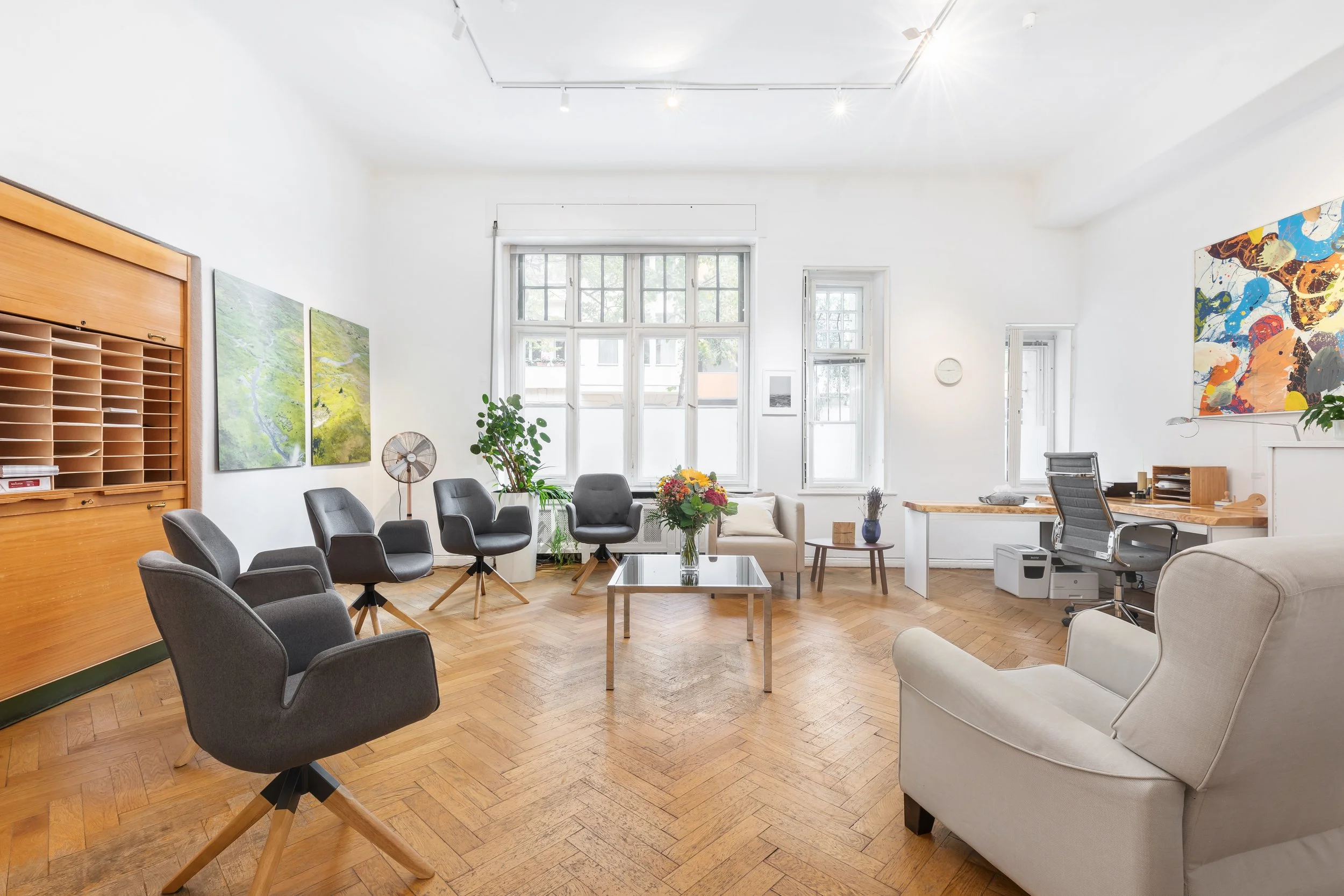 Heller, moderner Sitzungsraum mit großen Fenstern, 10 Stühlen, einem Sofa, Pflanzen und moderner Kunst an den Wänden.