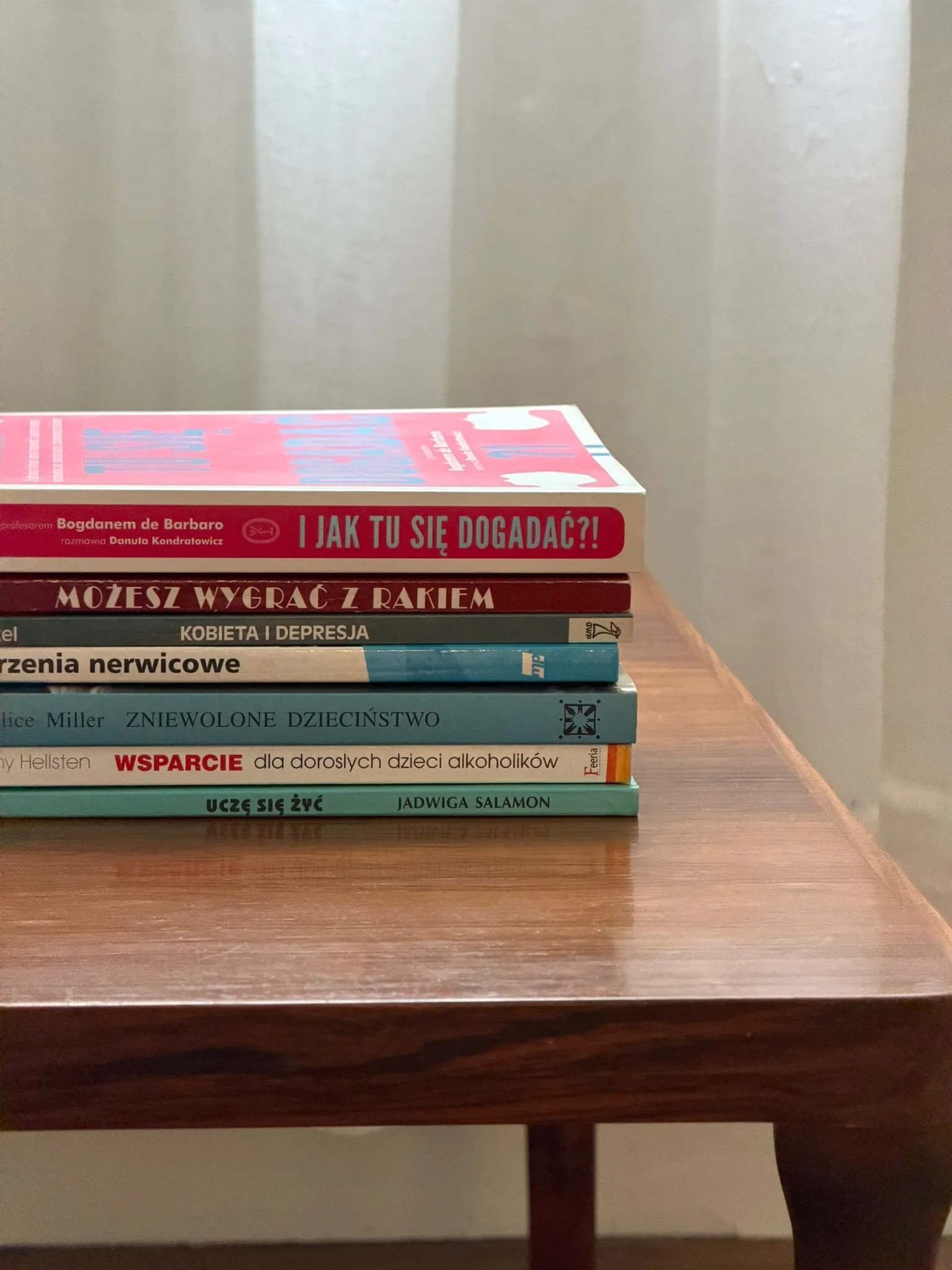 Stack of books on a wooden table with a plain gray wall in the background.