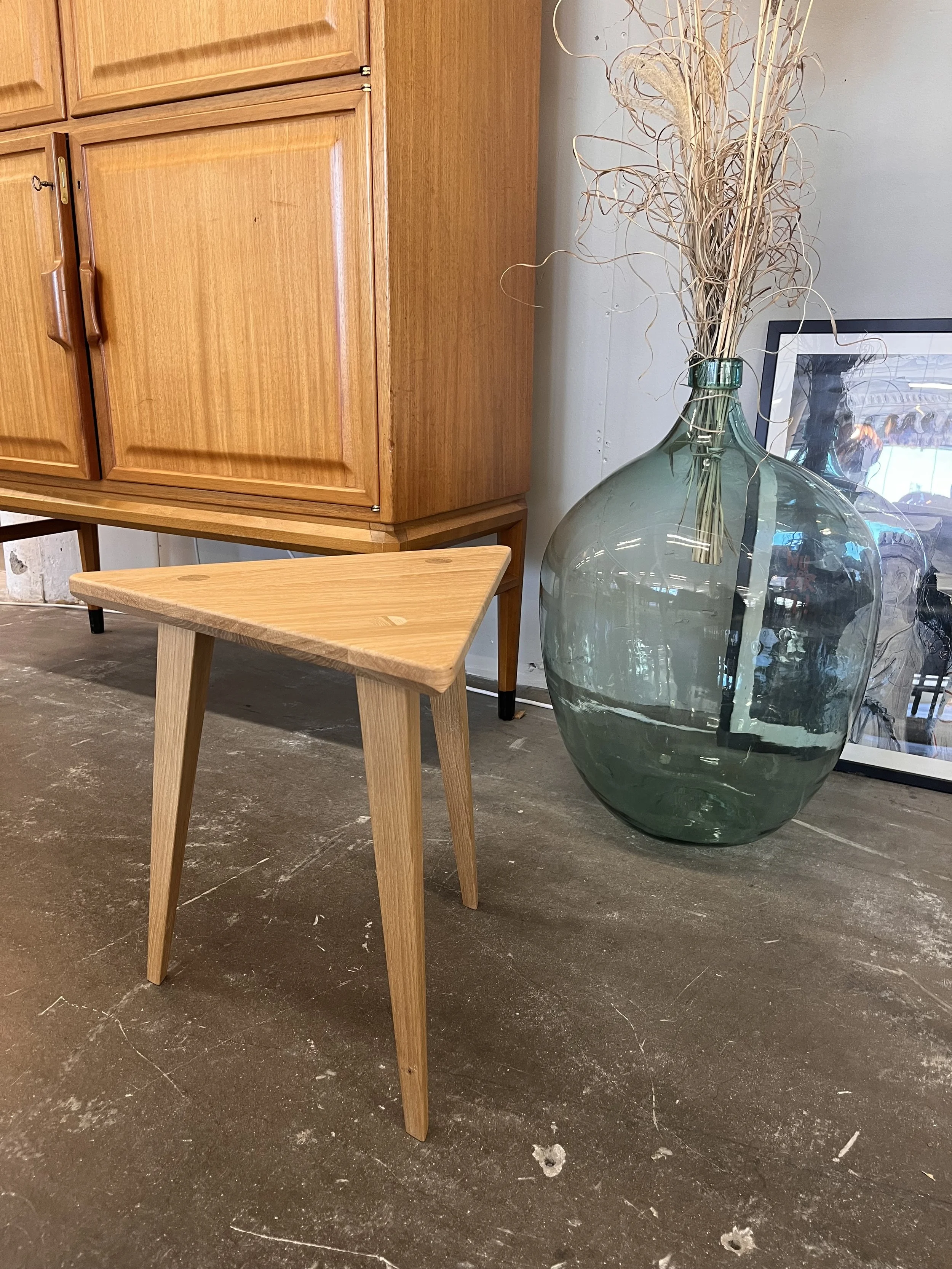 Glasvas med torra växter, träskåp och ett litet träbord placerat på en mörkgrått golv i ett inomhusrum.