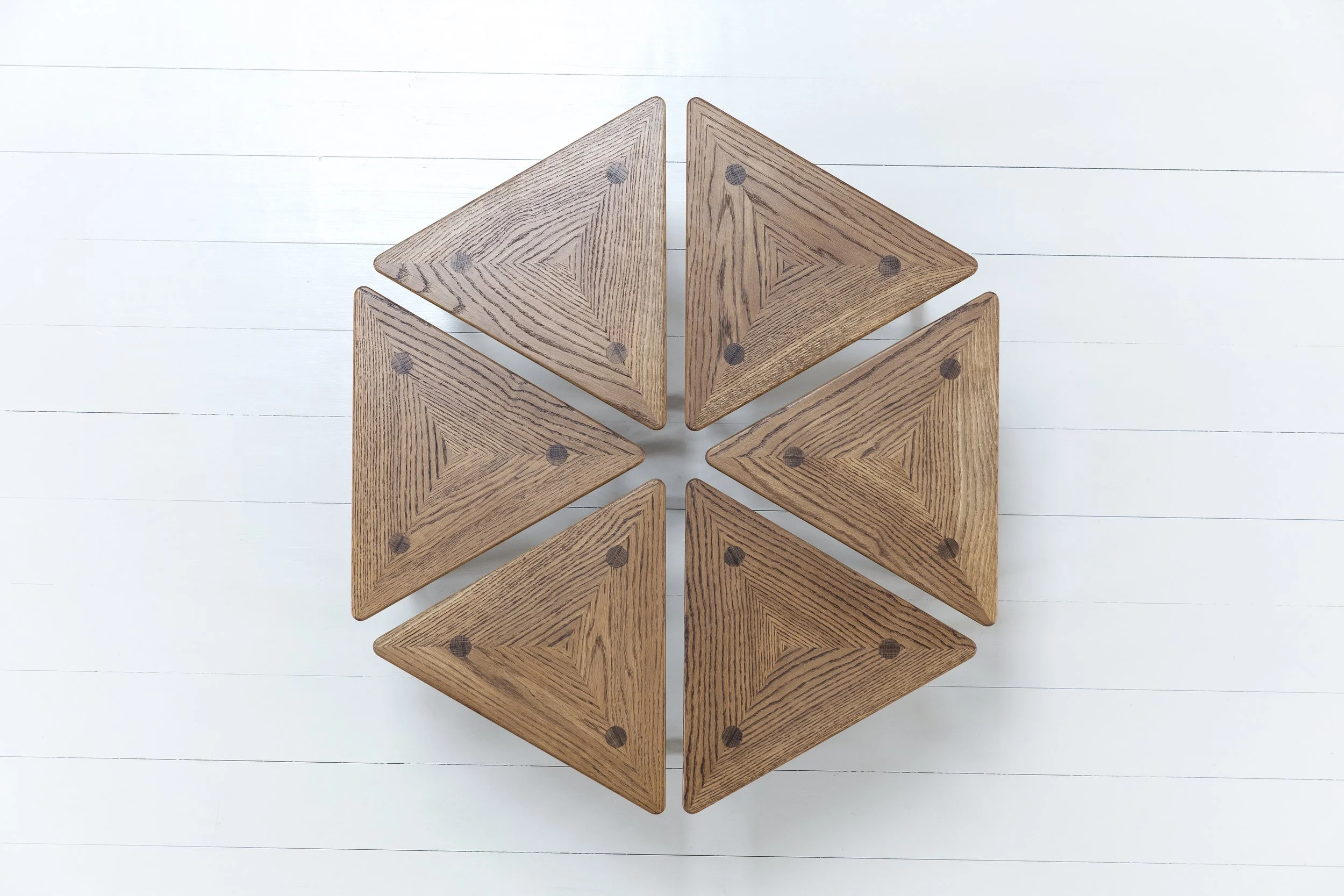 Sju träbitar formade som trianglar, placerade i en cirkel på en vit träbänksyta.