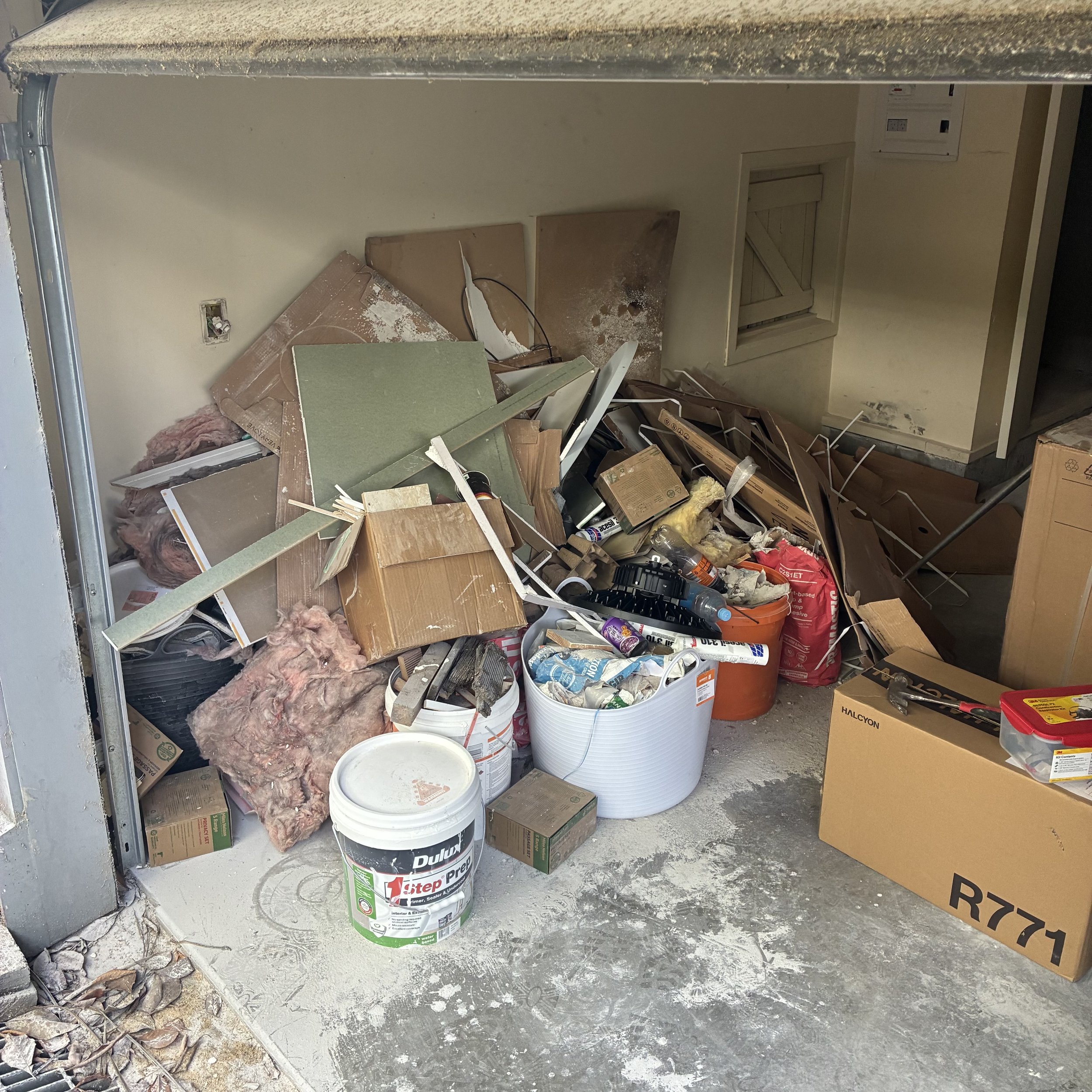 Construction site with scattered drywall, insulation, boxes, buckets, and miscellaneous building supplies.