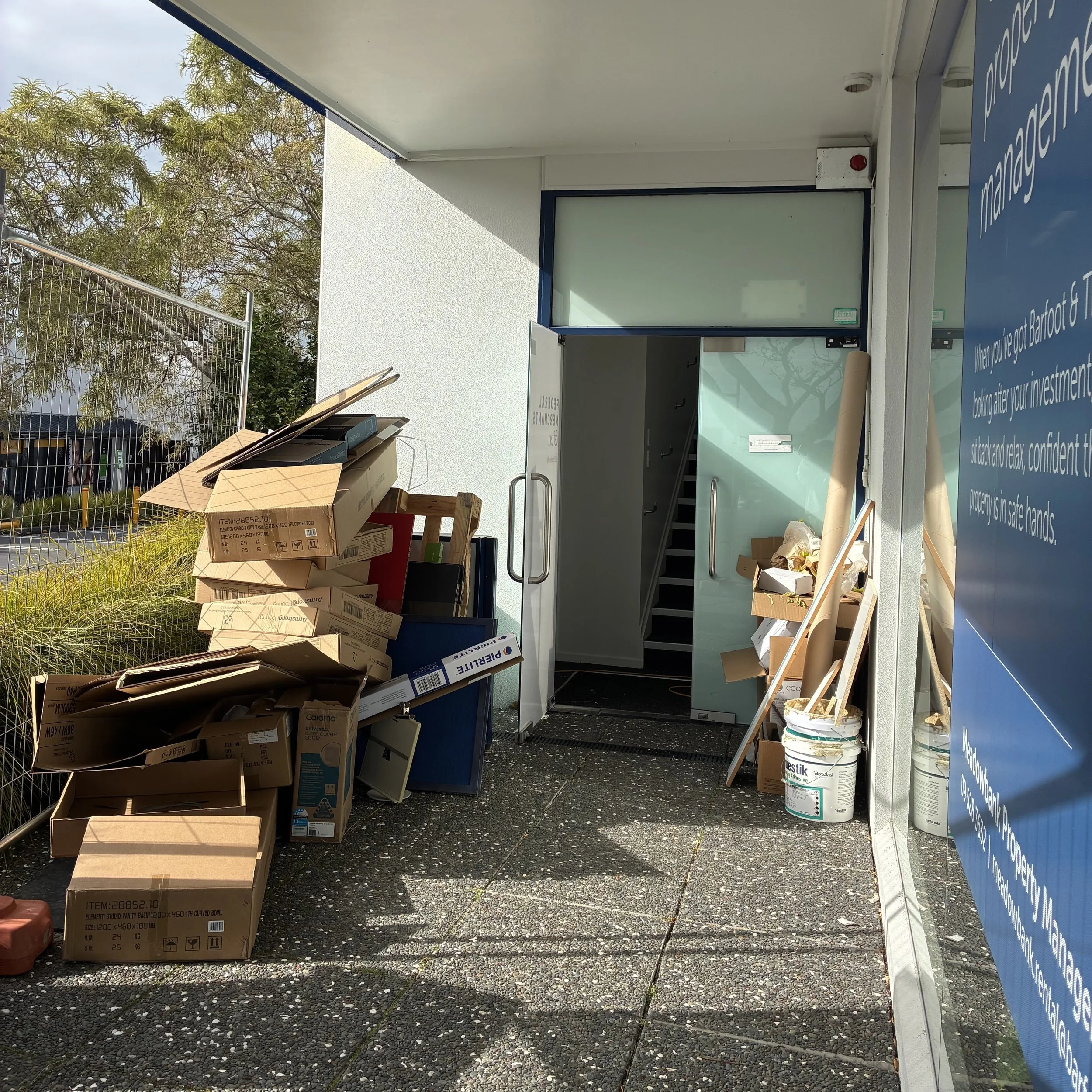 Stacked cardboard boxes near a door with a cart inside an outdoor space.