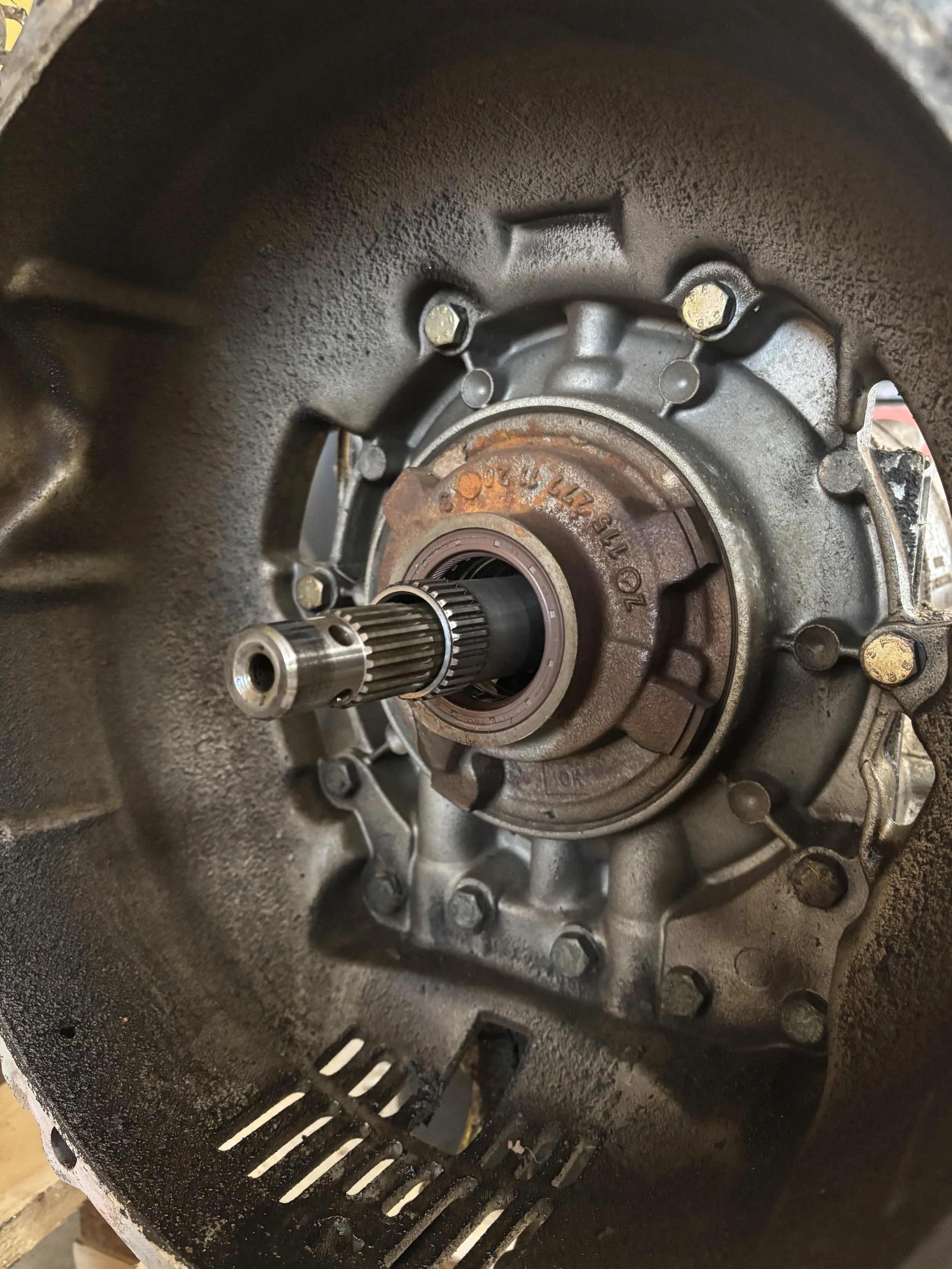 Inuti en metallisk cylindervägg med en splineskaft som sticker ut och är delvis rostig, omgiven av en ring av fastskruvade metallbultar.