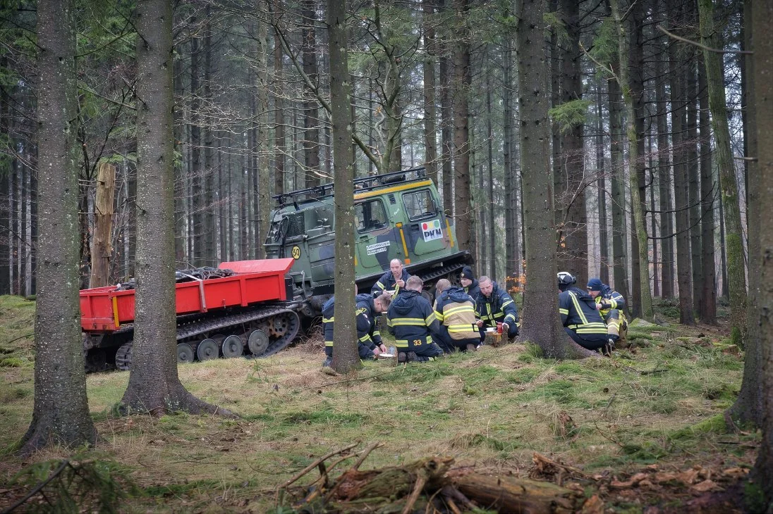 Brandmän i skogssammandragning efter en skogsincident, med ett traktorliknande fordon i bakgrunden.