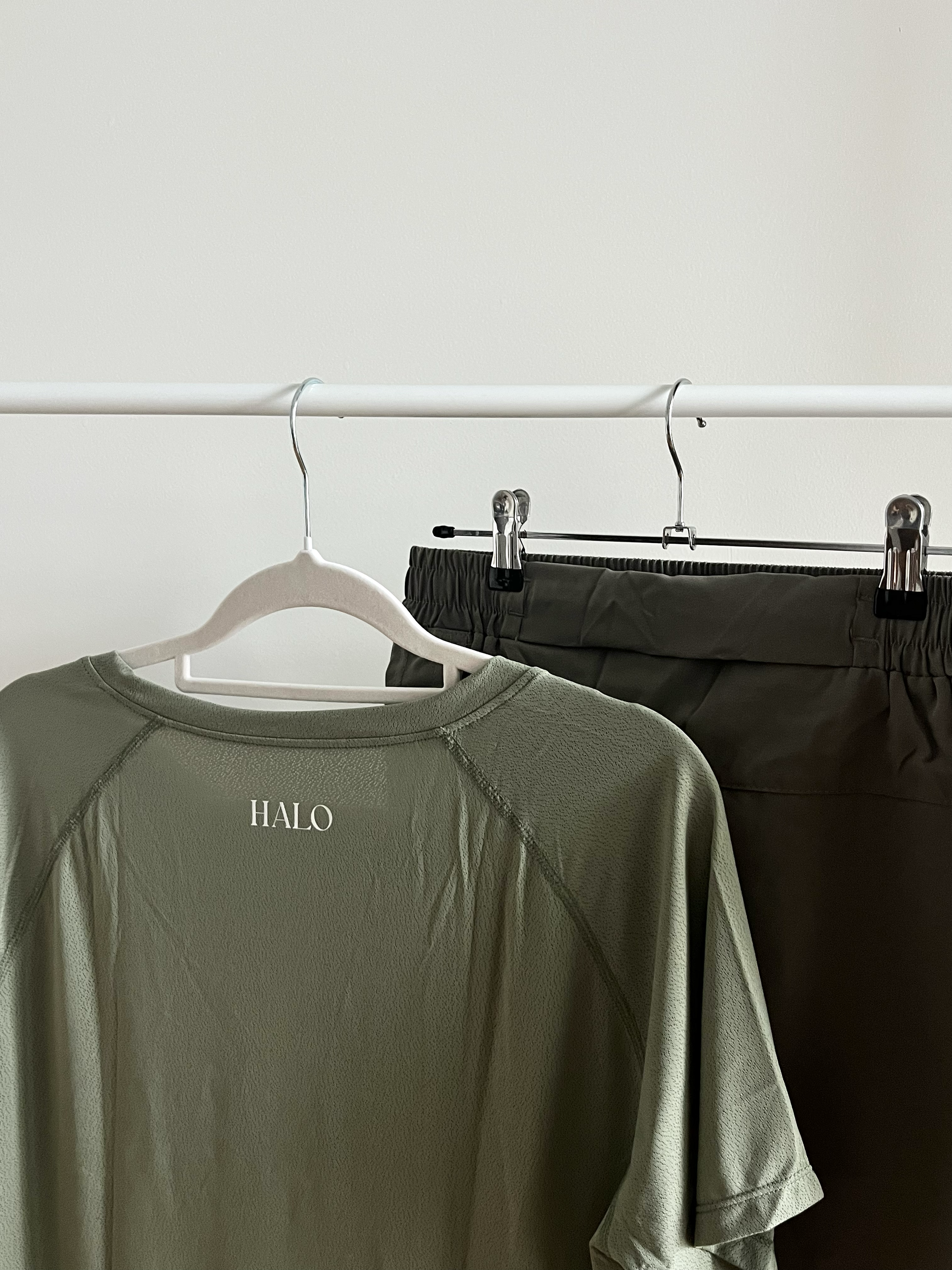A white clothing rack holding a green mens activewear shirt