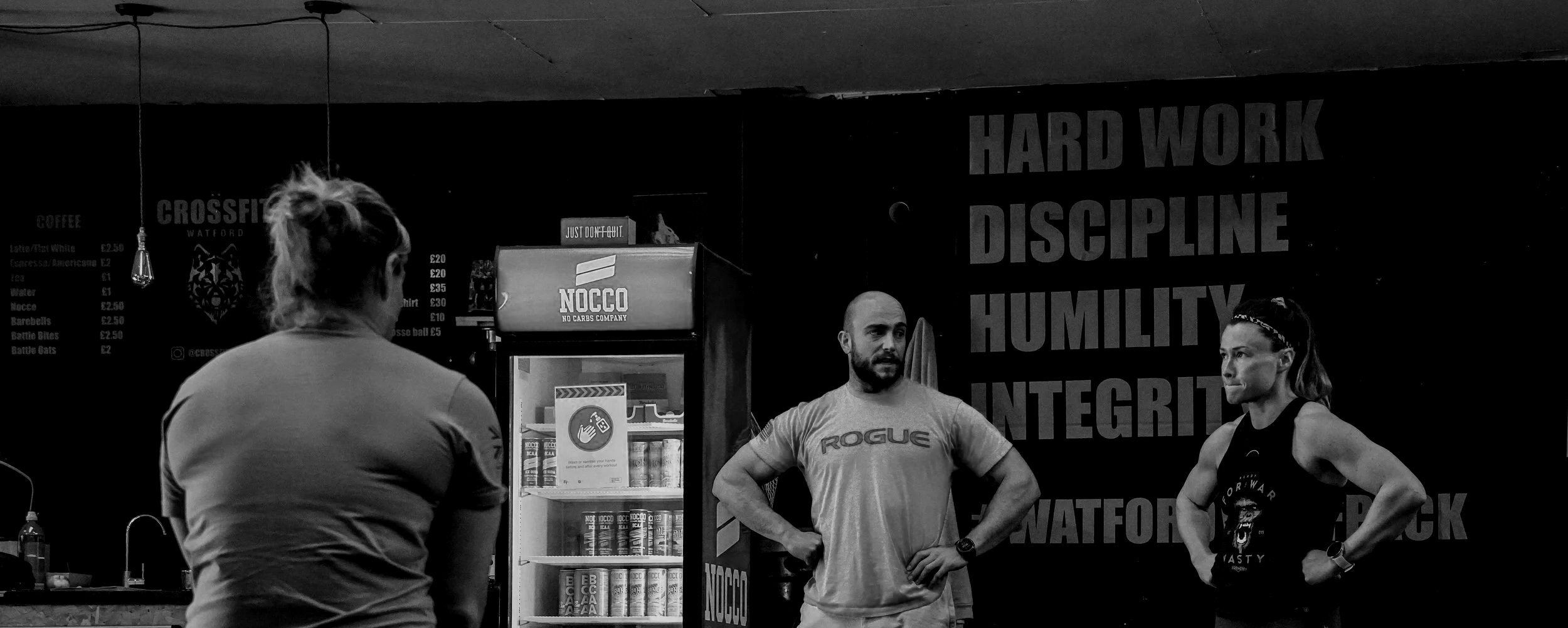 A coach with a group of athletes in a CrossFit gym, debriefing a workout performance and providing coaching feedback.