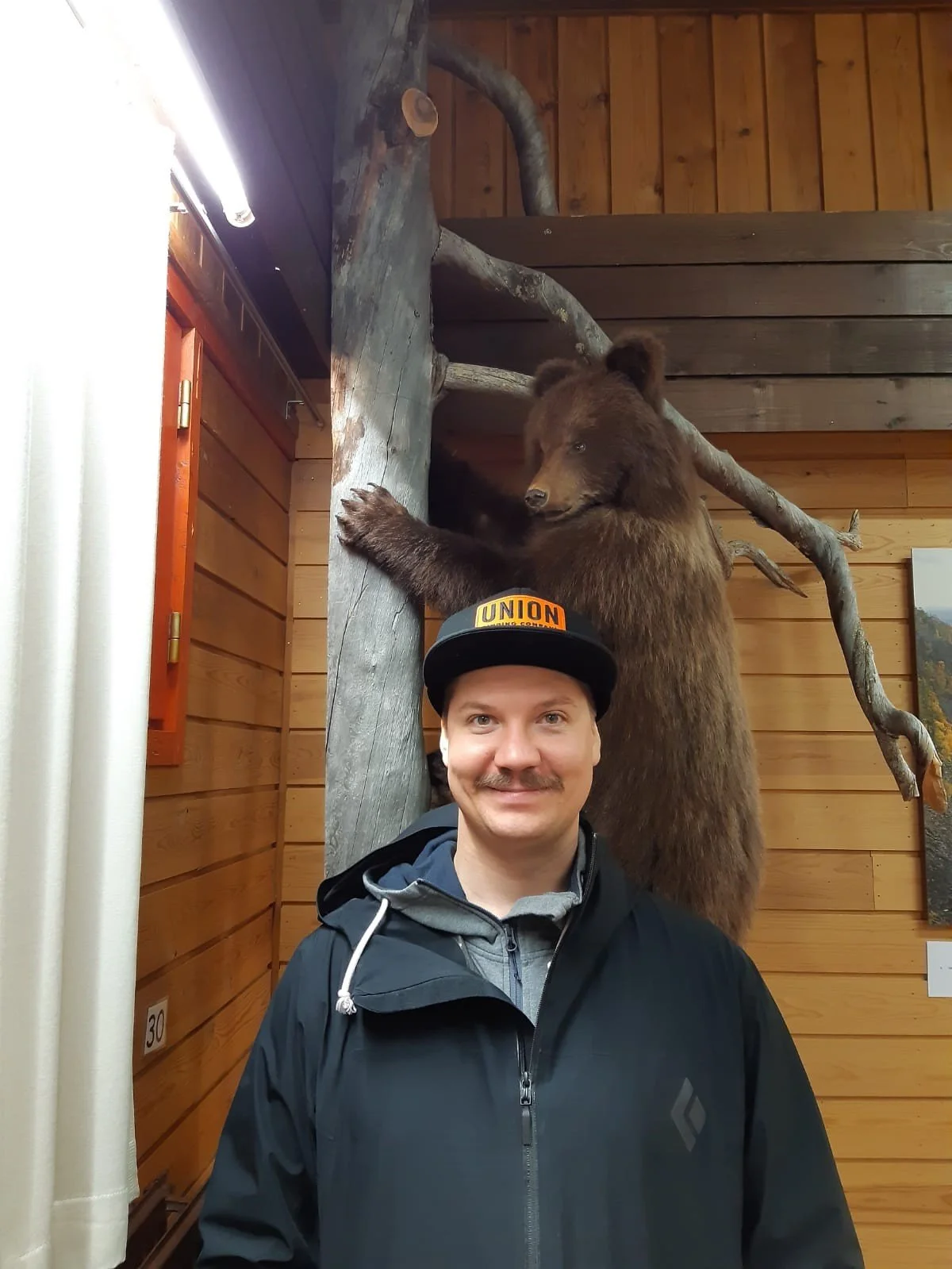 Mies hymyilee valokuvassa, seisoen kameran edessä. 