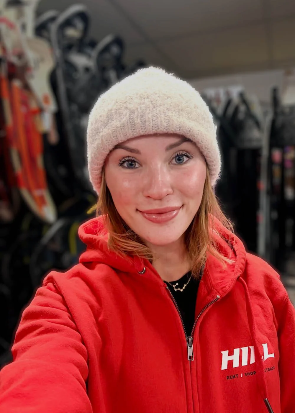 Nuori nainen keskustan lumisessa urheiluvälinemyymälässä, jossa on talviurheiluvälineitä taustalla.