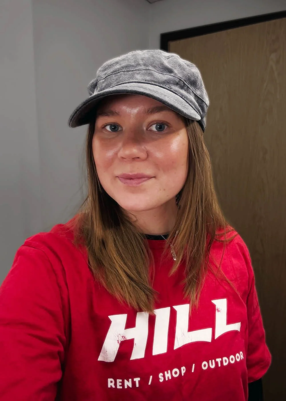 Nuori nainen, päällä harmaa lippalakki ja punainen HILL-brändin collegepaita.