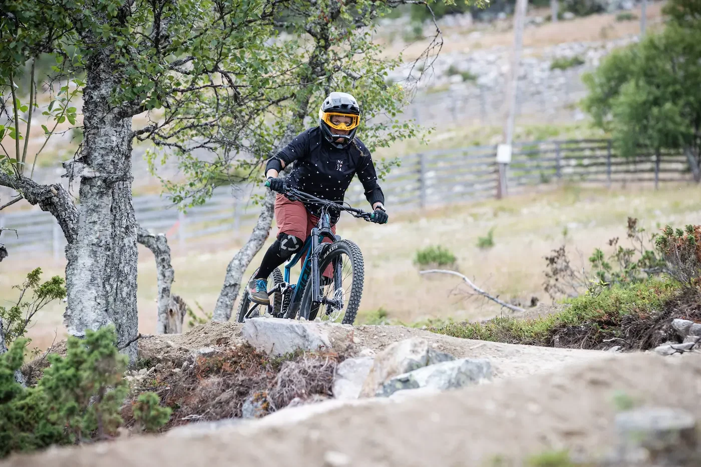 Mies mountain biking polulla maastossa, ympärillä puita ja luonnonmaisema.