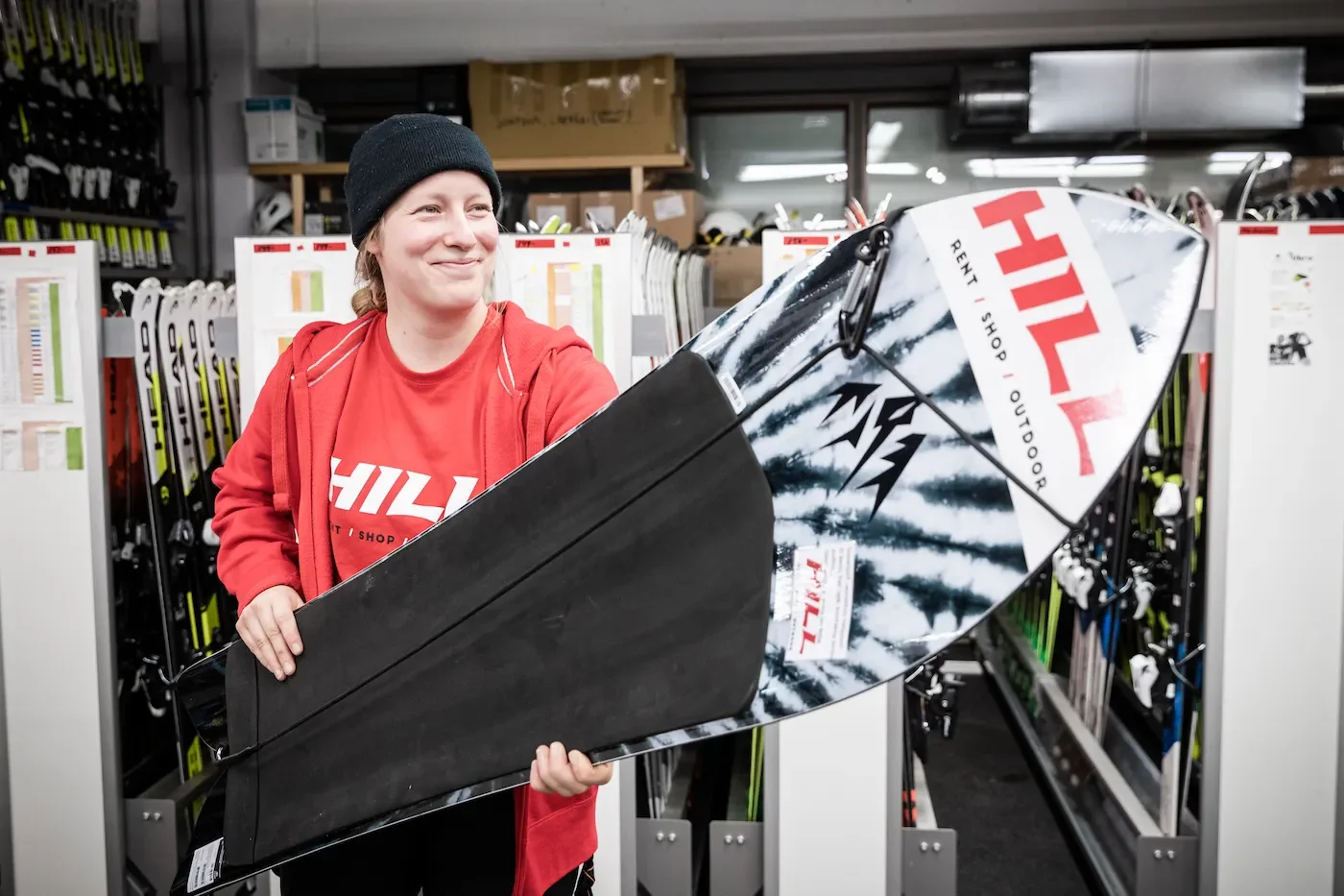 Nainen on punaisessa hupparissa ja mustassa pipossa. Ojentaa lumisurf-lautaa.