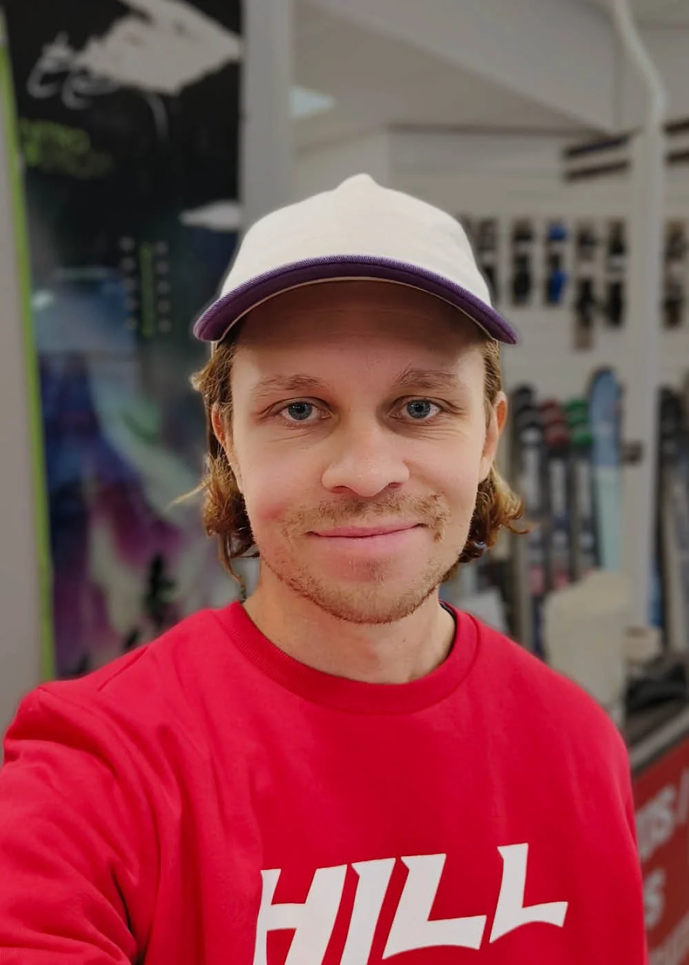 Nuori mies ottaa selfieä urheiluvälinemyymälässä, hänellä on päässä valkoinen lippalakki ja punainen t-paita.