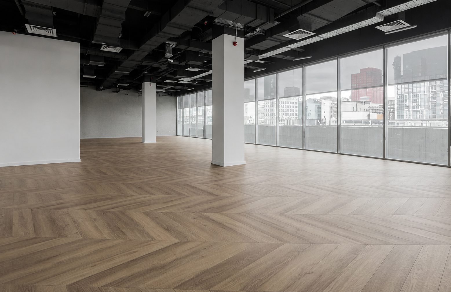 Empty office space with large windows, wooden flooring, white walls, and a black ceiling with exposed ductwork.