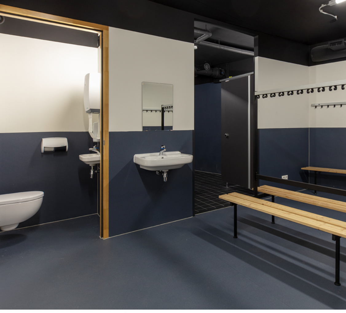 A modern, clean locker room with benches, sinks, toilets, and a changing area.