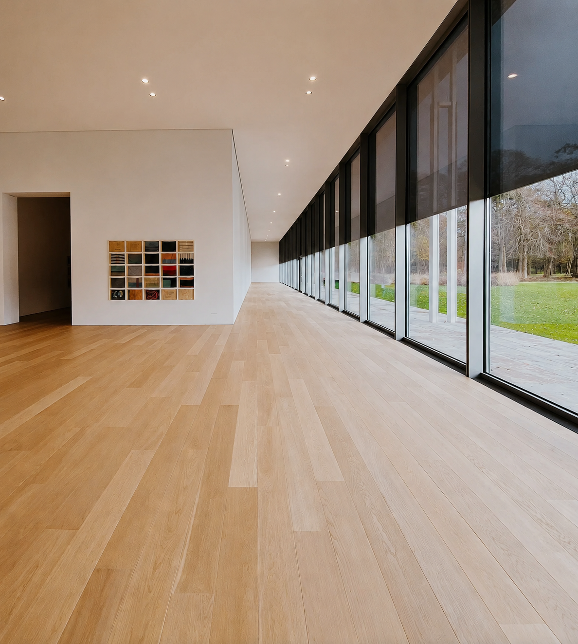 Modern interior with wooden flooring and floor-to-ceiling windows showing outdoor greenery.