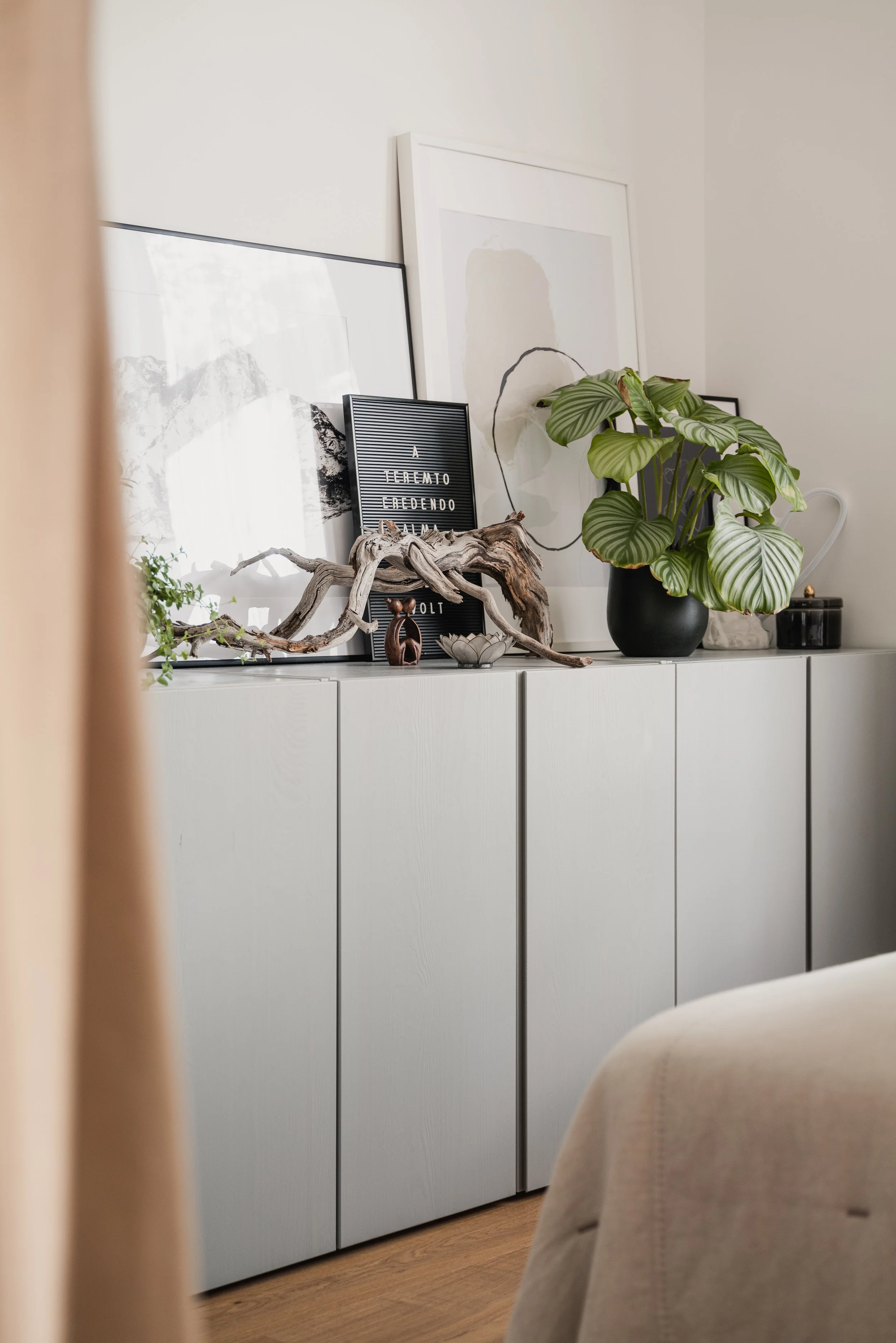 Decorative shelf with framed artwork, a piece of driftwood, a small sculpture, a potted plant, and other decorative objects against a white wall.
