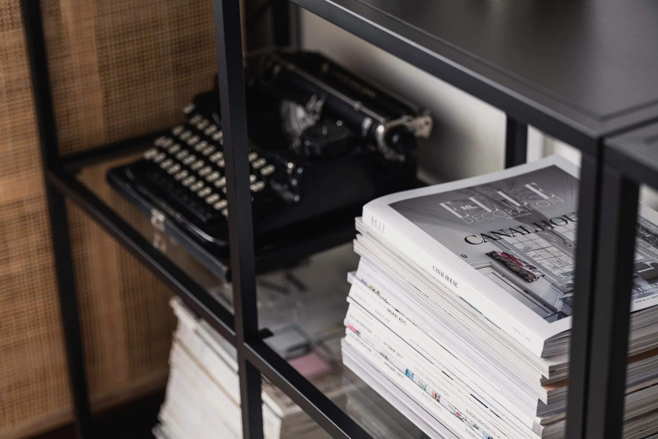 A black metal shelving unit with a vintage black typewriter and a stack of magazines or books.