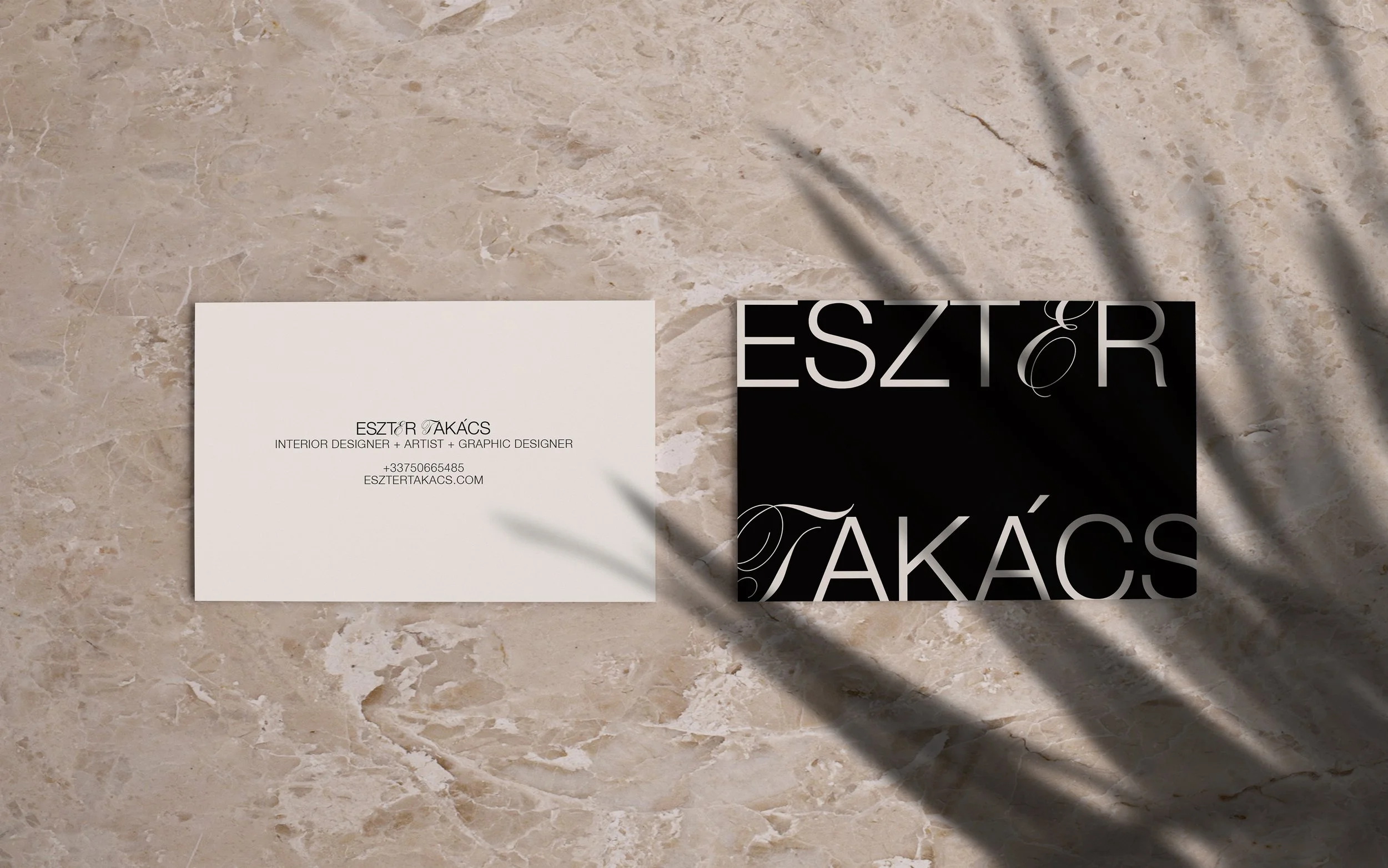 Business cards on a marble surface. One card reads 'ESZTER TAKÁCS Interior Designer + Artist + Graphic Designer +33670665485 esztertakacs.com'. The other card has the name 'ESZTER' in large white letters on a black background with a decorative flourish.