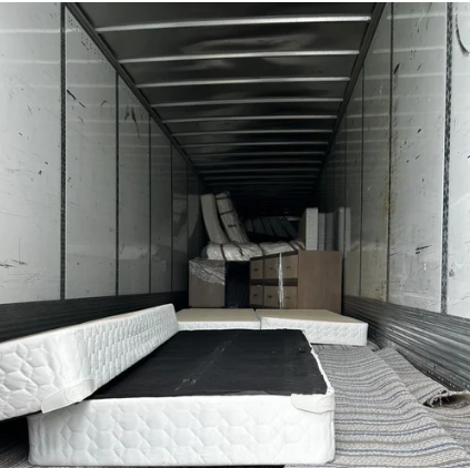 Interior of an empty shipping container filled with mattresses and boxes.