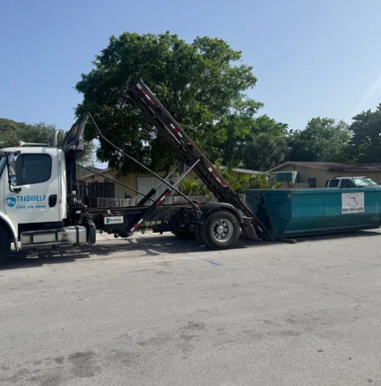 A garbage truck with a raised hydraulic arm lifting a large blue dumpster on a suburban street.