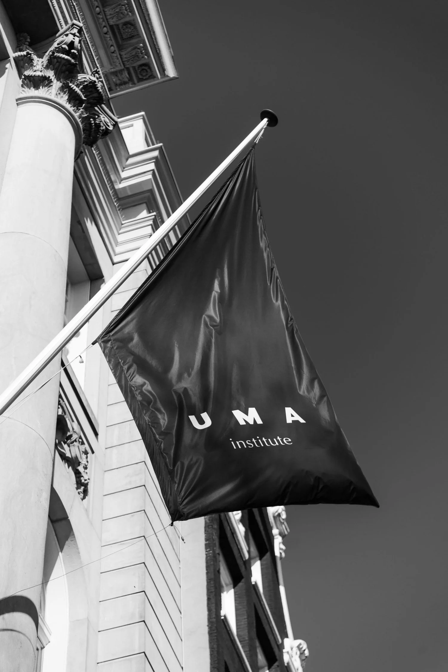 Black flag with the words 'UMA institute' hanging outside a historic building with detailed architecture.