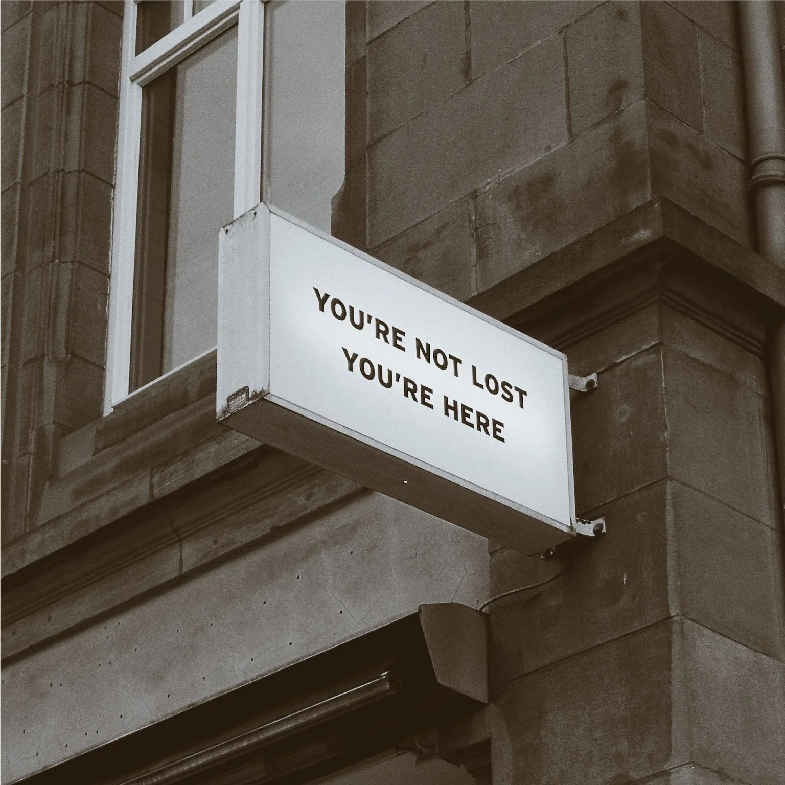 A street sign on a brick building that reads, 'YOU'RE NOT LOST YOU'RE HERE'.