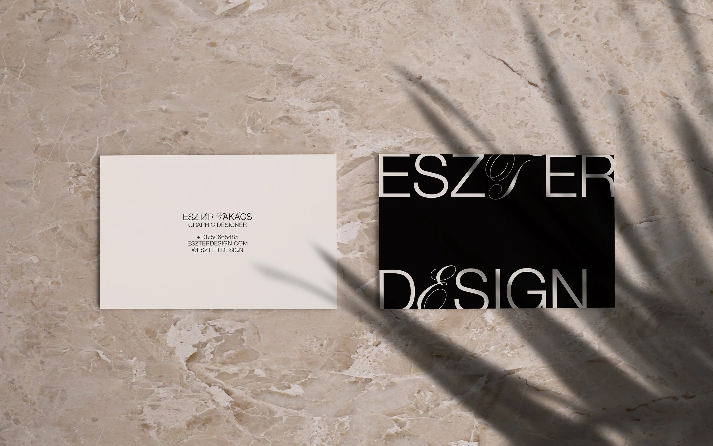 Business cards on a marble surface, one white with contact information and one black with the word 'DESIGN' in large letters. Designed by Eszter Takacs, graphic designer.