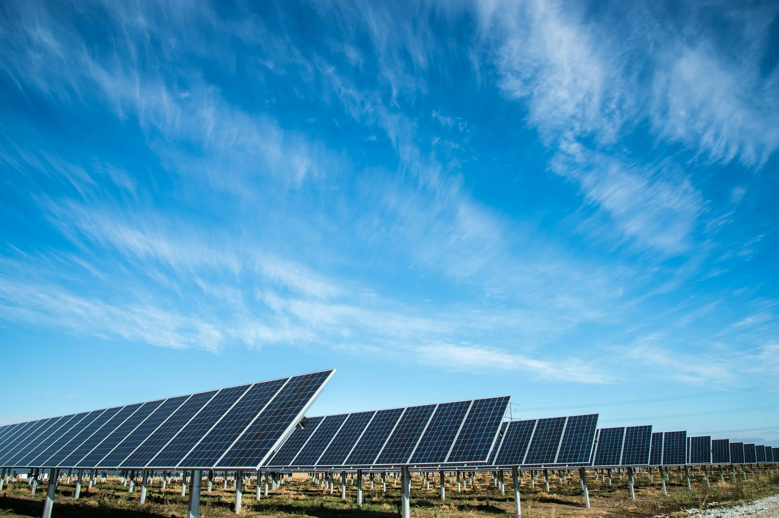 Photovoltaic solar panels installed outdoors with a bright blue sky and wispy clouds above.