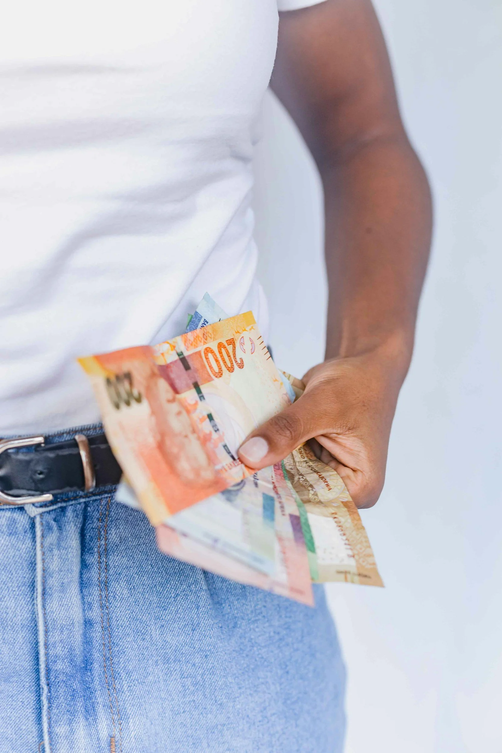 A person holding Australian currency notes in front of their body, wearing a white shirt and blue jeans.