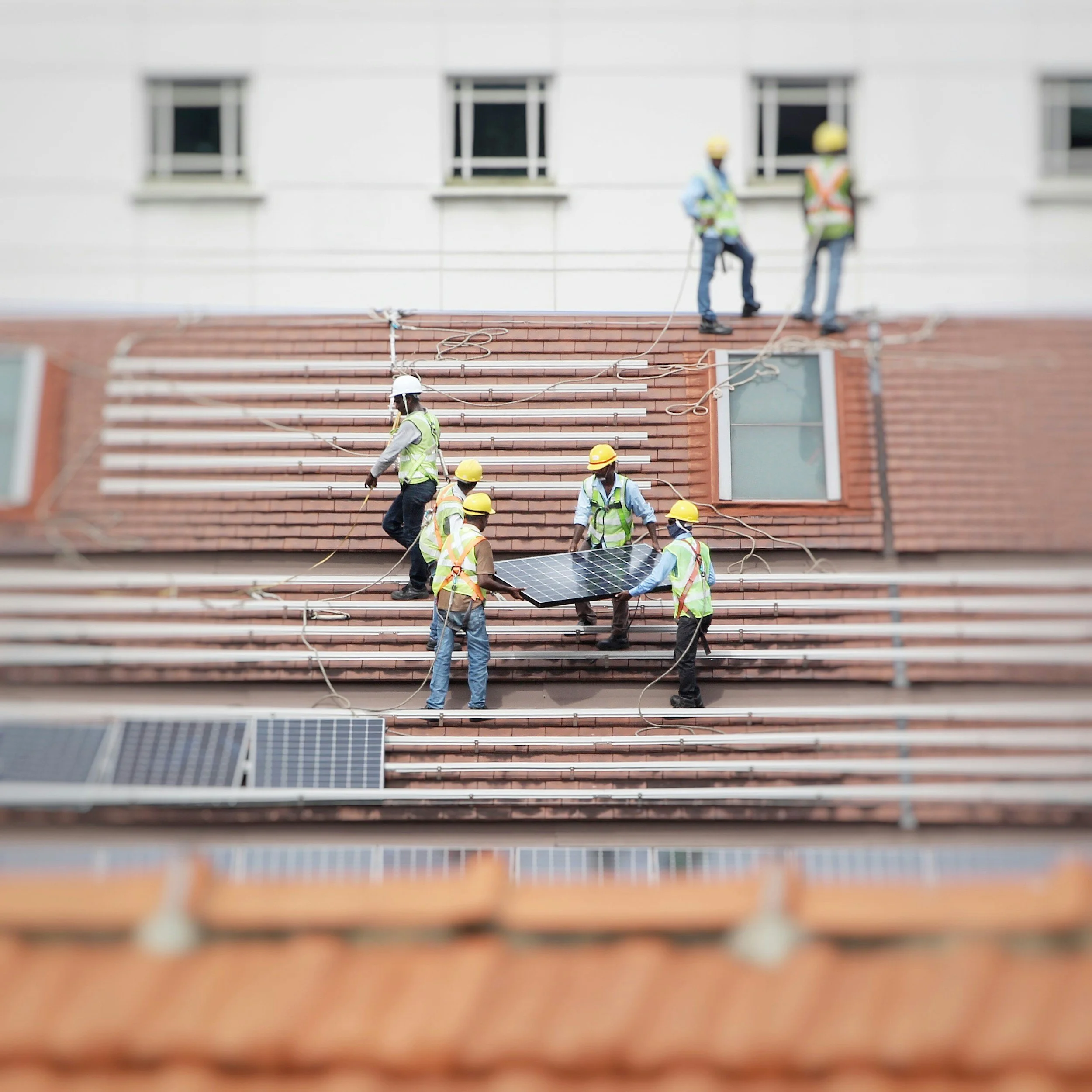 Workers installing solar panels on a residential roof, wearing safety gear and vests.