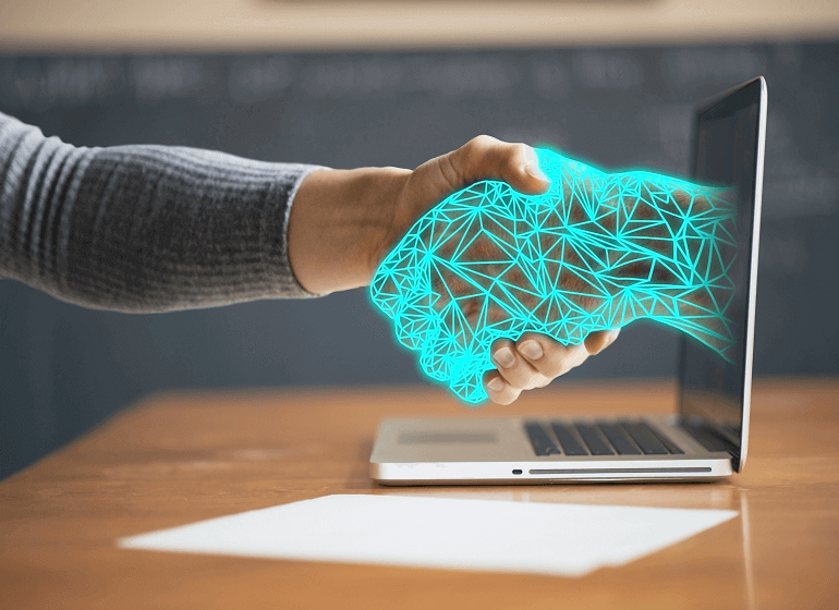 Person shaking hands with a digital hologram of a neural network emerging from a laptop.