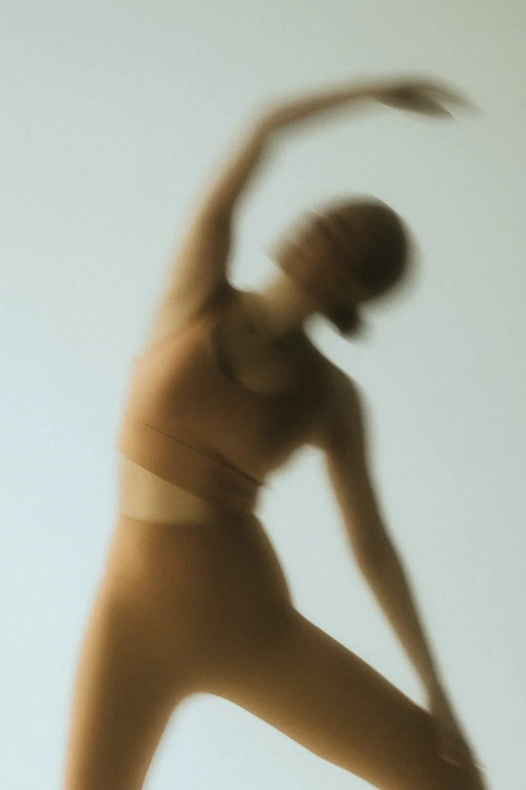 Blurred silhouette of a woman stretching against a plain light-colored background.