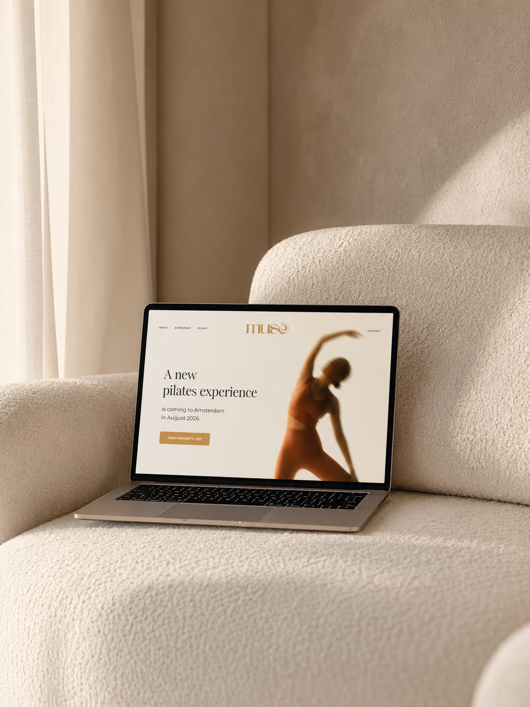 Laptop on a beige sofa displaying a website for a Pilates studio called Muse, with an image of a woman stretching.