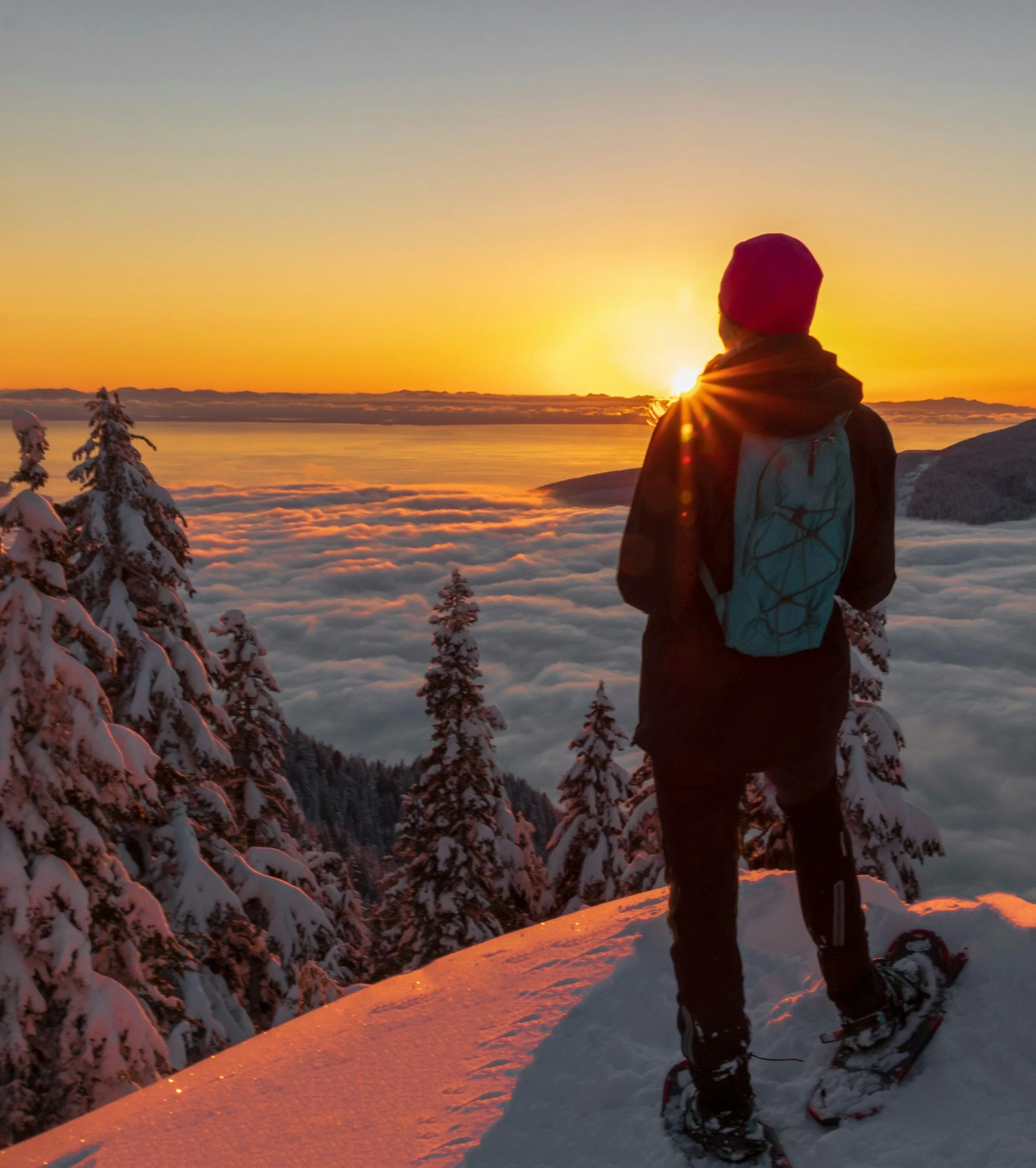 A person standing on a snowy mountain at sunrise overlooking the clouds below — the Inversion Leadership metaphor for clarity above complexity