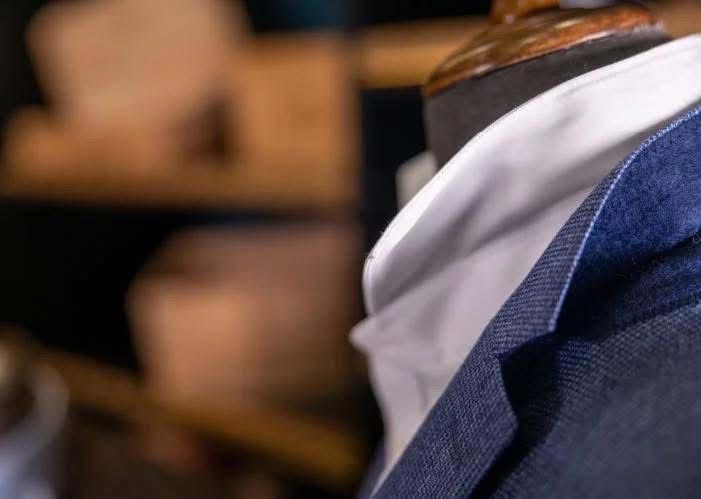 Une personne portant une chemise blanche et une veste bleue, avec une sculpture en haut de la tête dans un environnement intérieur.