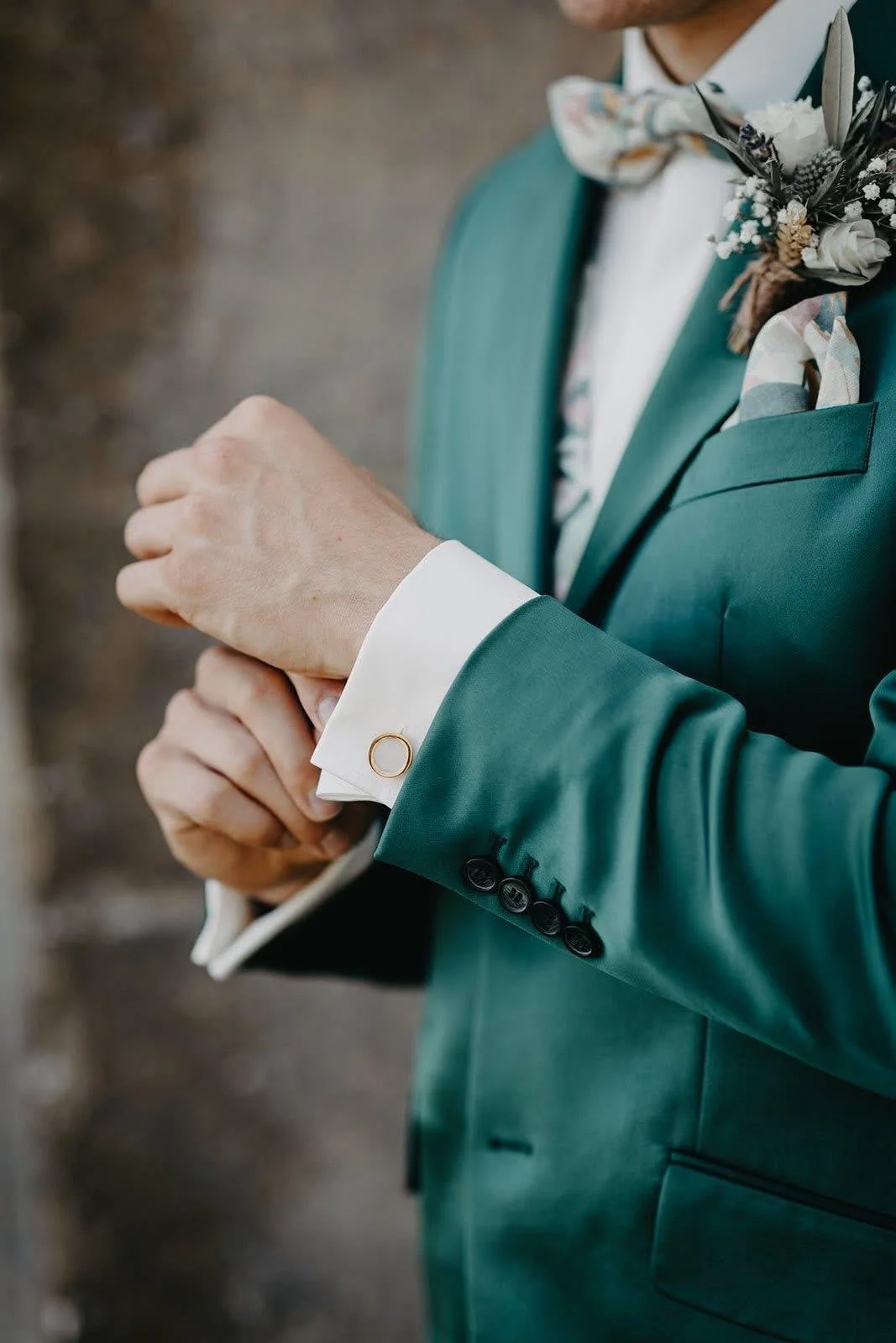 Close-up d’un homme en costume vert ajustant ses manchettes et portant une boutonnière de mariage.